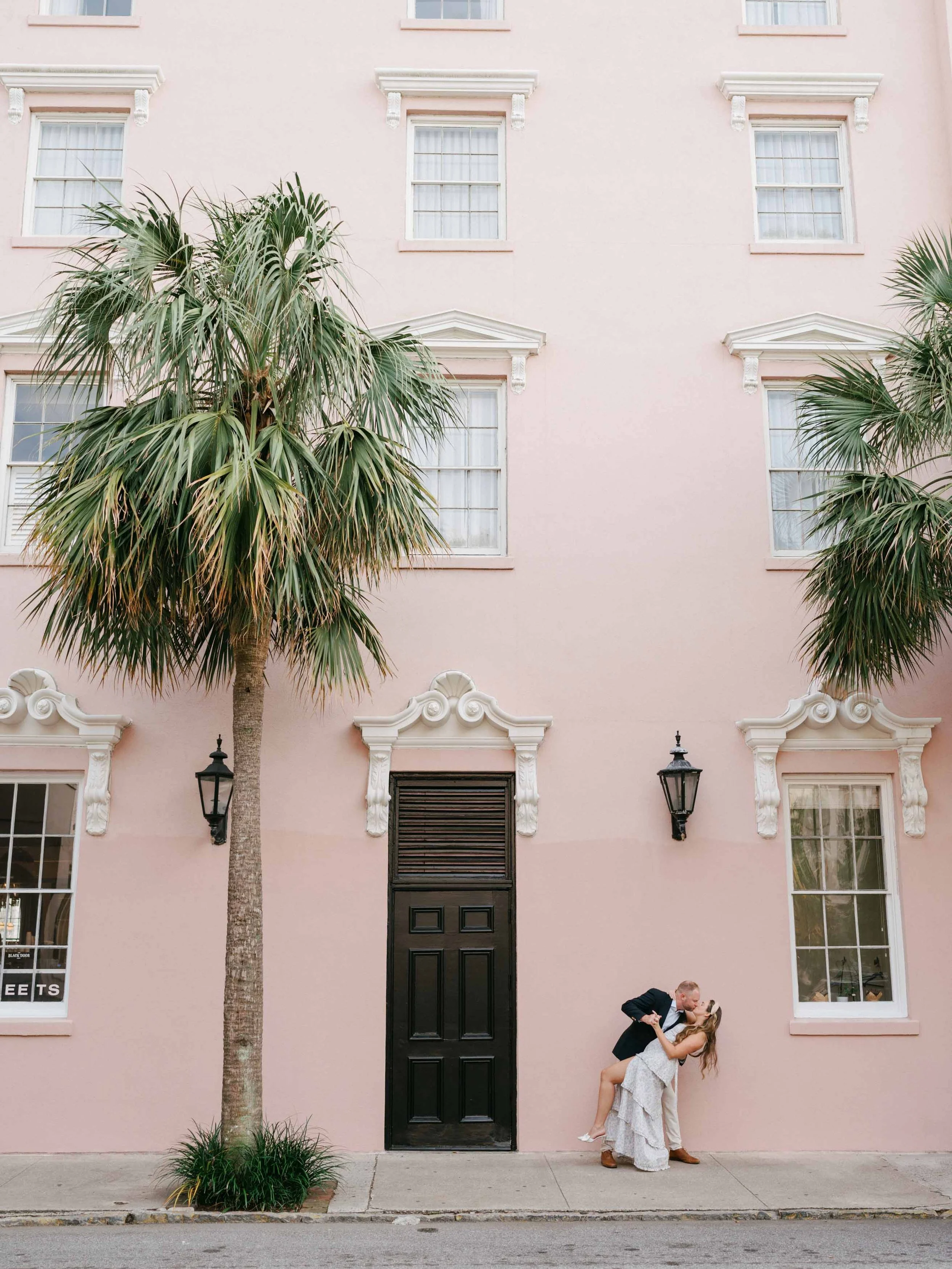 Couple dancing in front of a pink building with tall palm trees in downtown Charleston, SC.