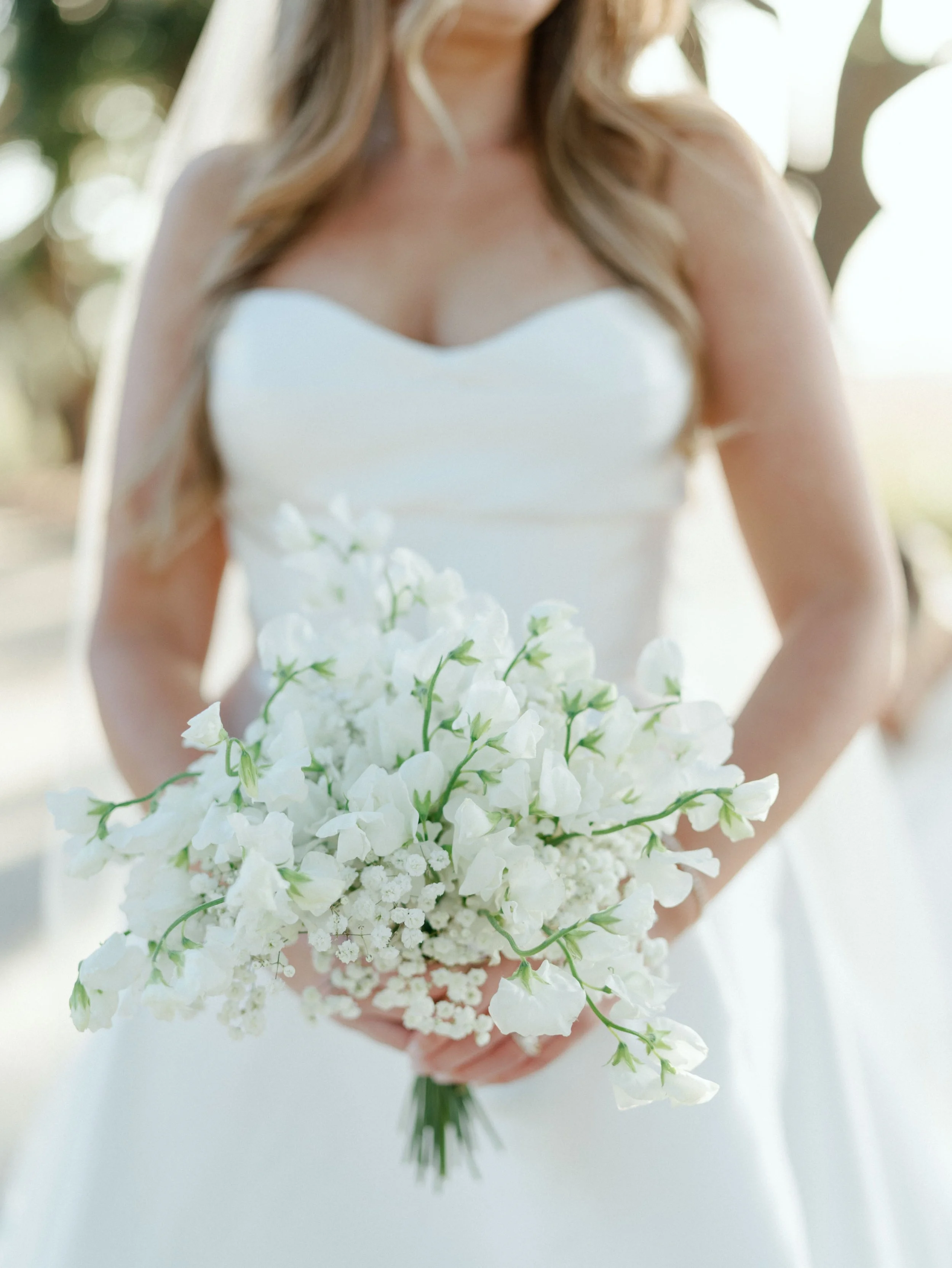 A woman in a strapless white wedding dress holding a bouquet of white flowers.