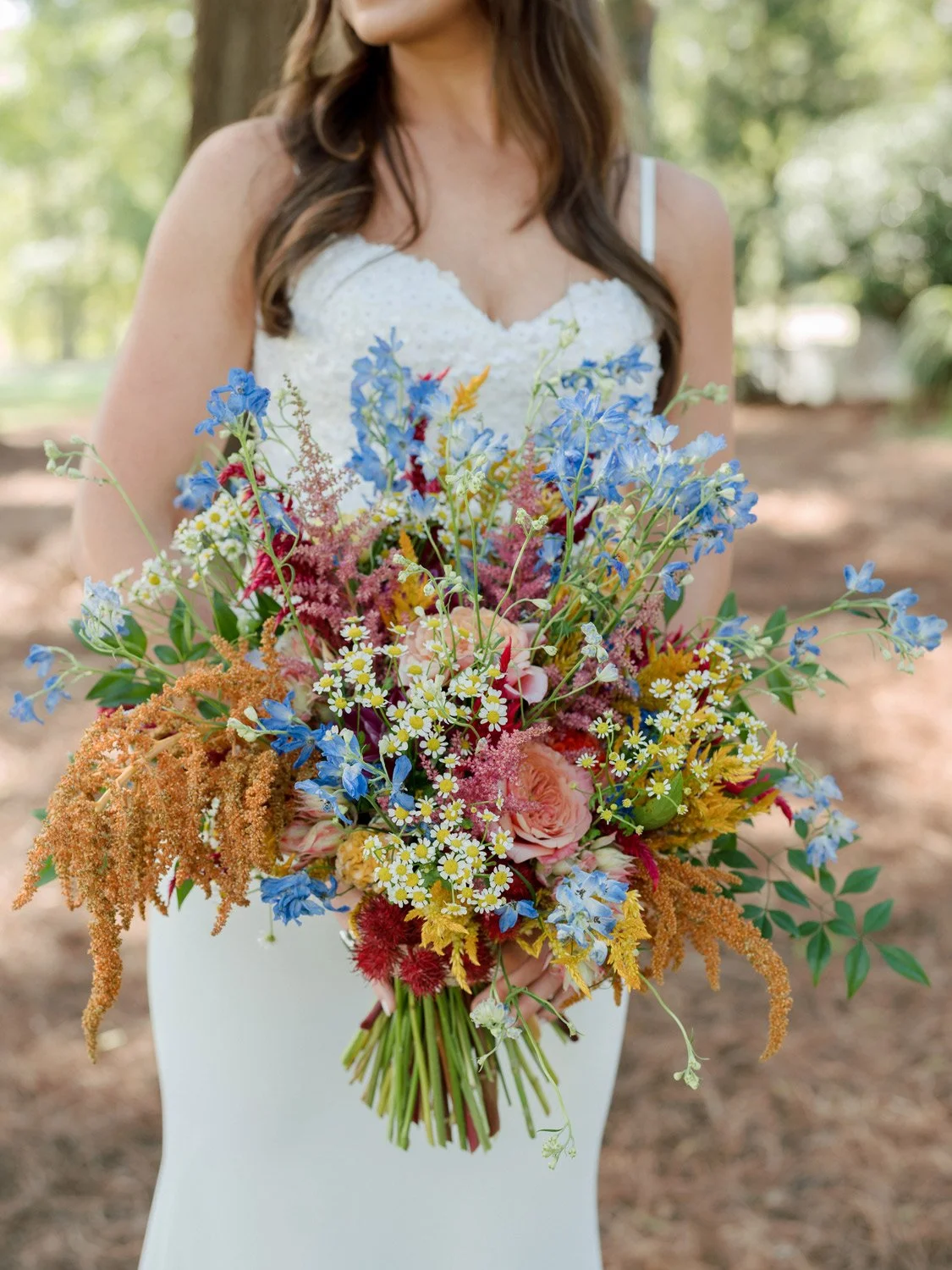Brunette woman in white dress holding a colorful bouquet of various flowers outdoors.