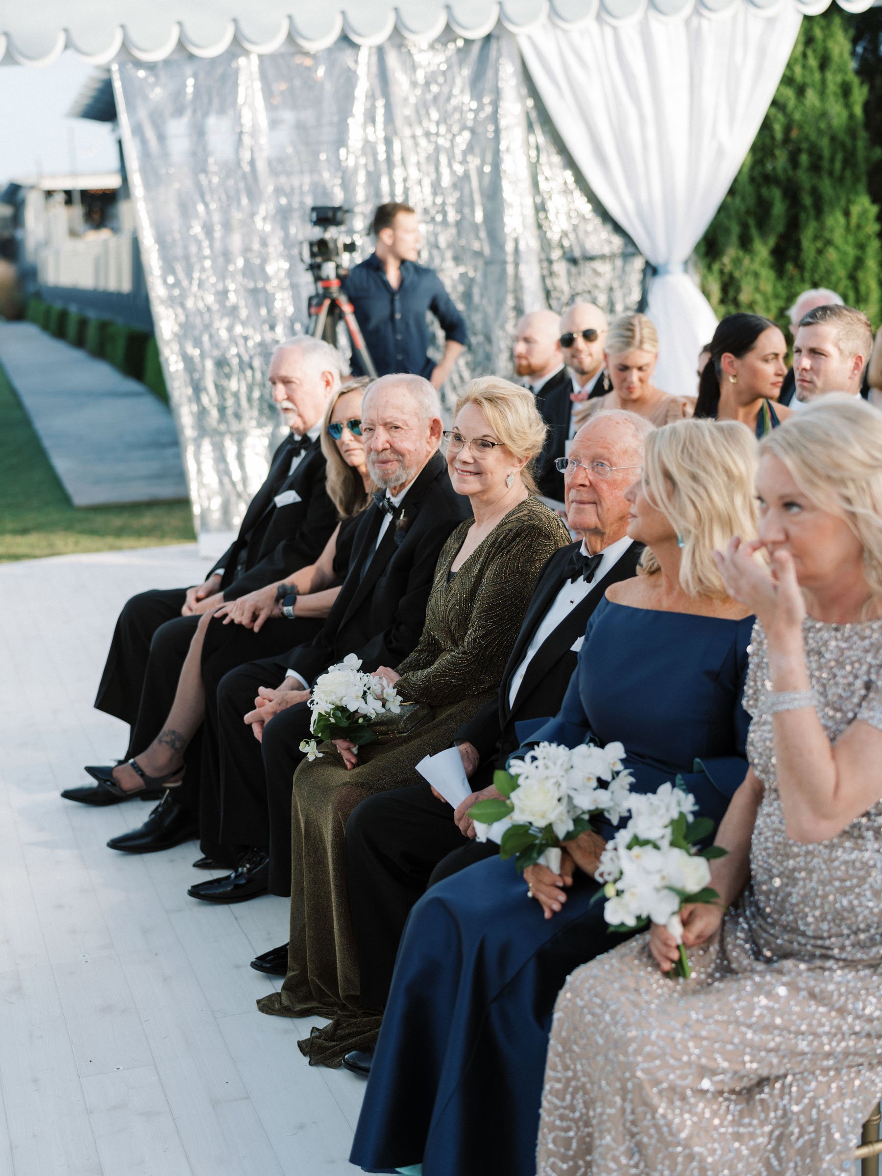Attendees sitting in a row at an outdoor wedding ceremony.