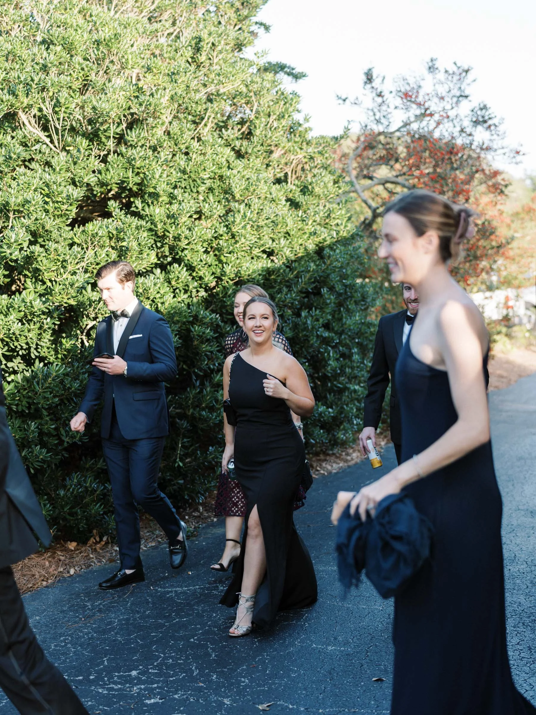 Group of people dressed in formal attire walking outdoors on a sunny day.