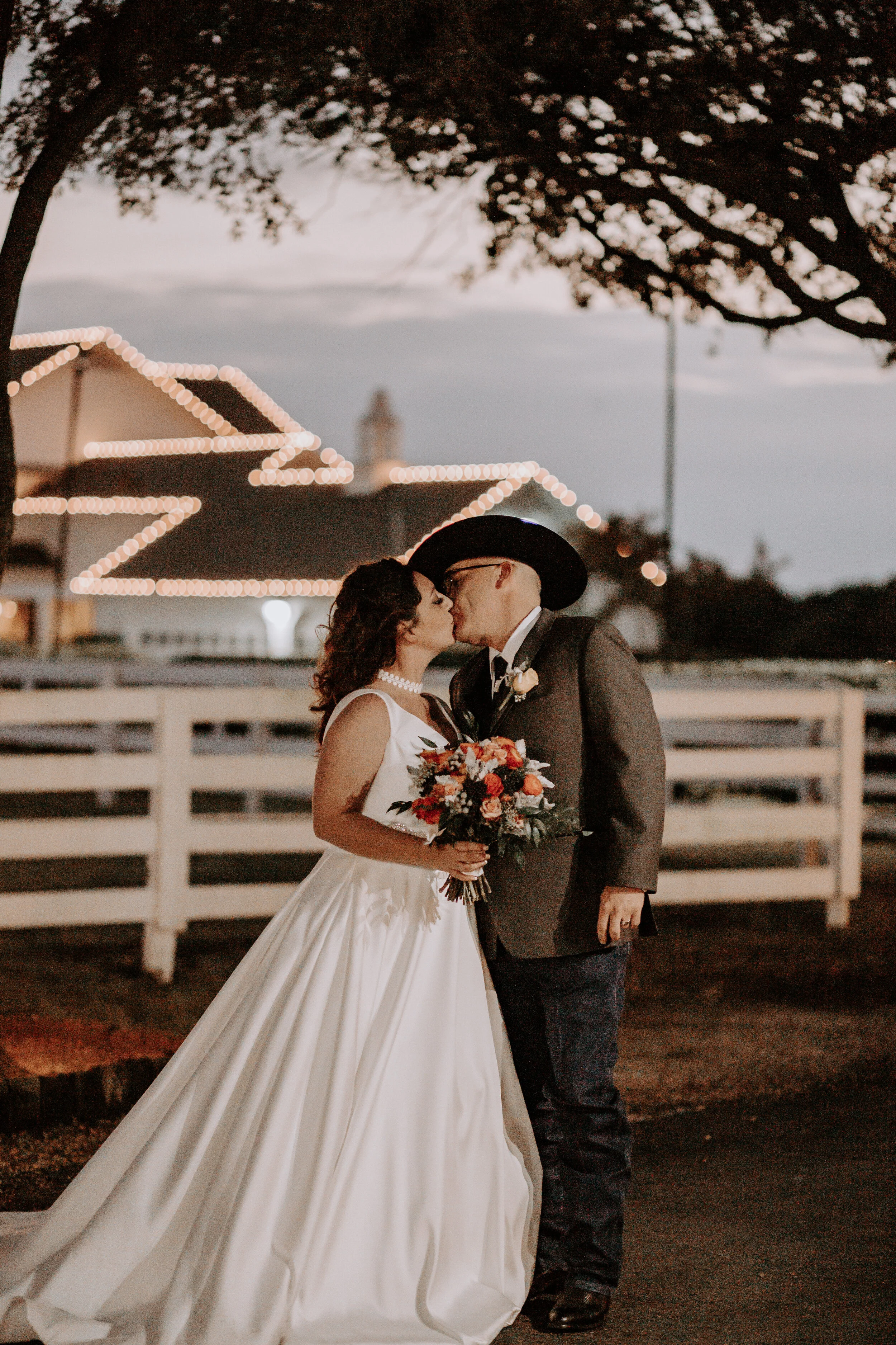 man and woman kiss in front of fence and house