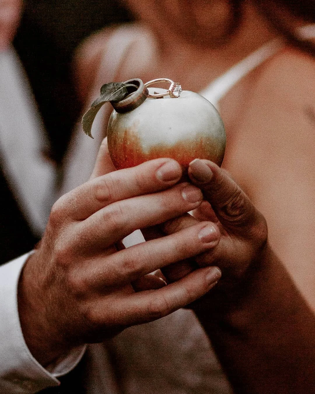 man and woman hold apple with rings on stem