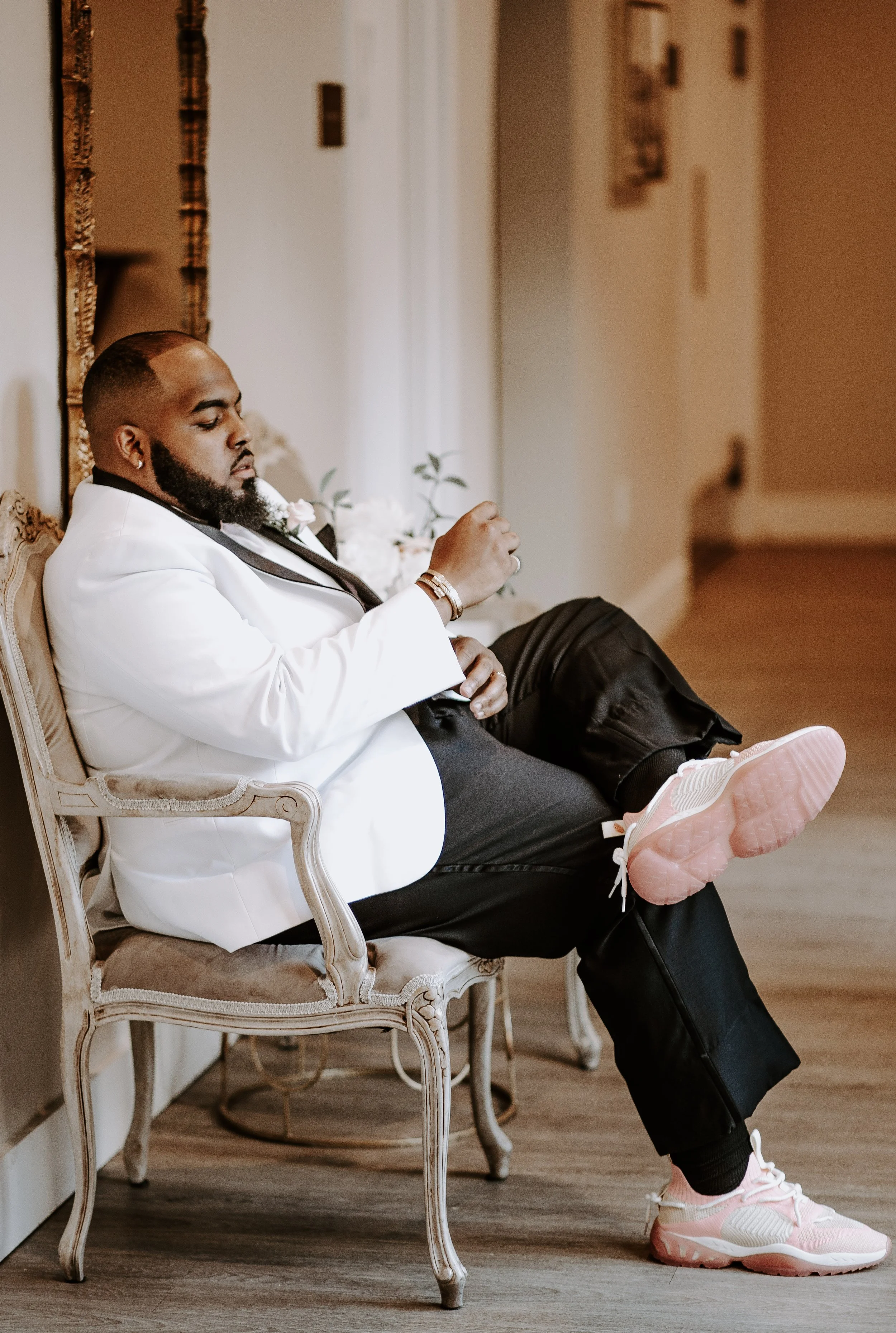 man sits in chair adjusting cufflink with leg crossed to show off shoes