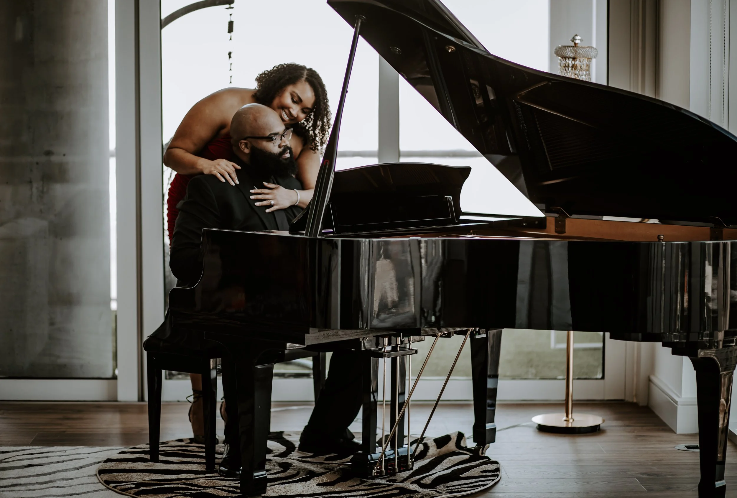 man seated at piano with woman hugging him from behind