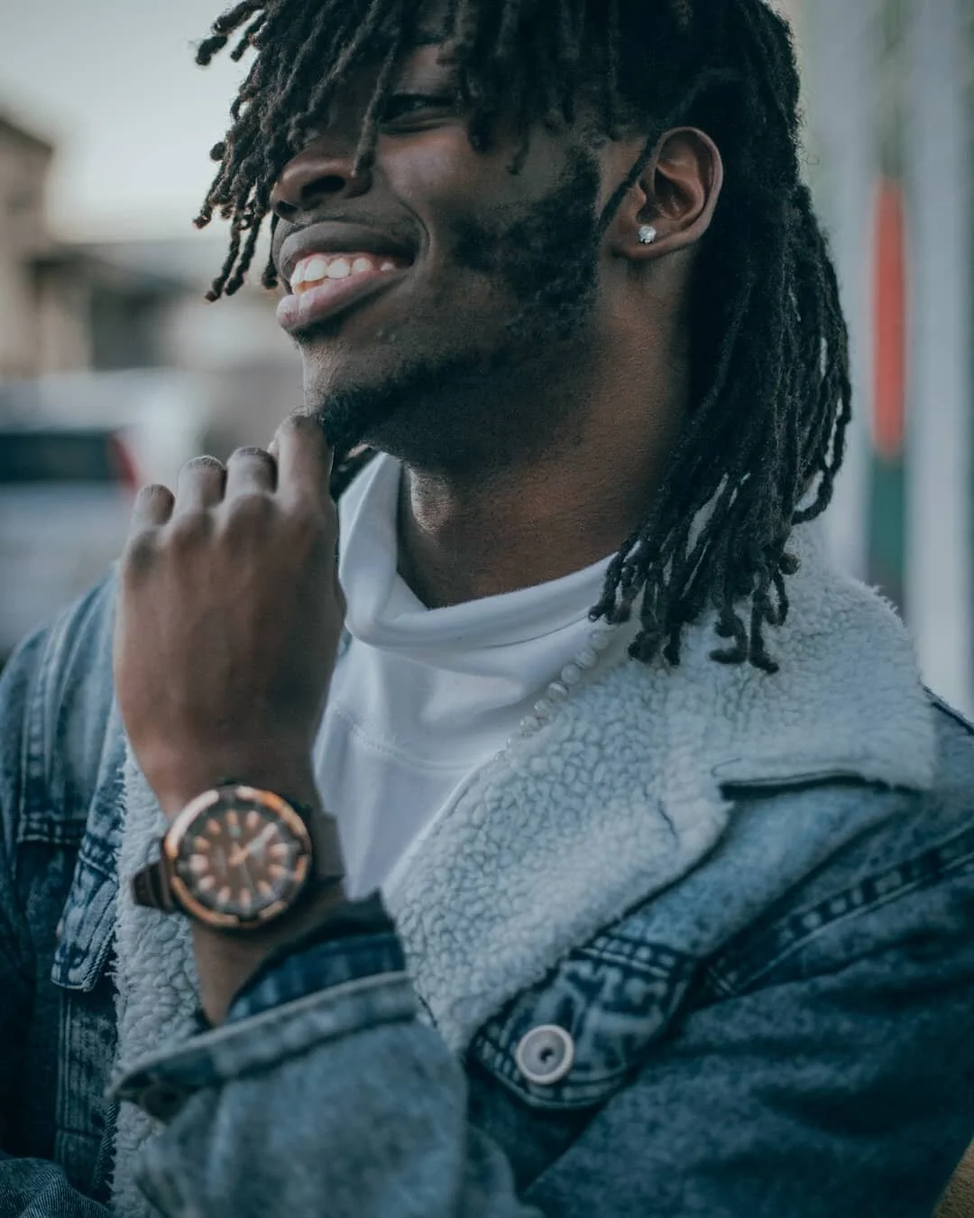 man holds chin hair while smiling to display watch