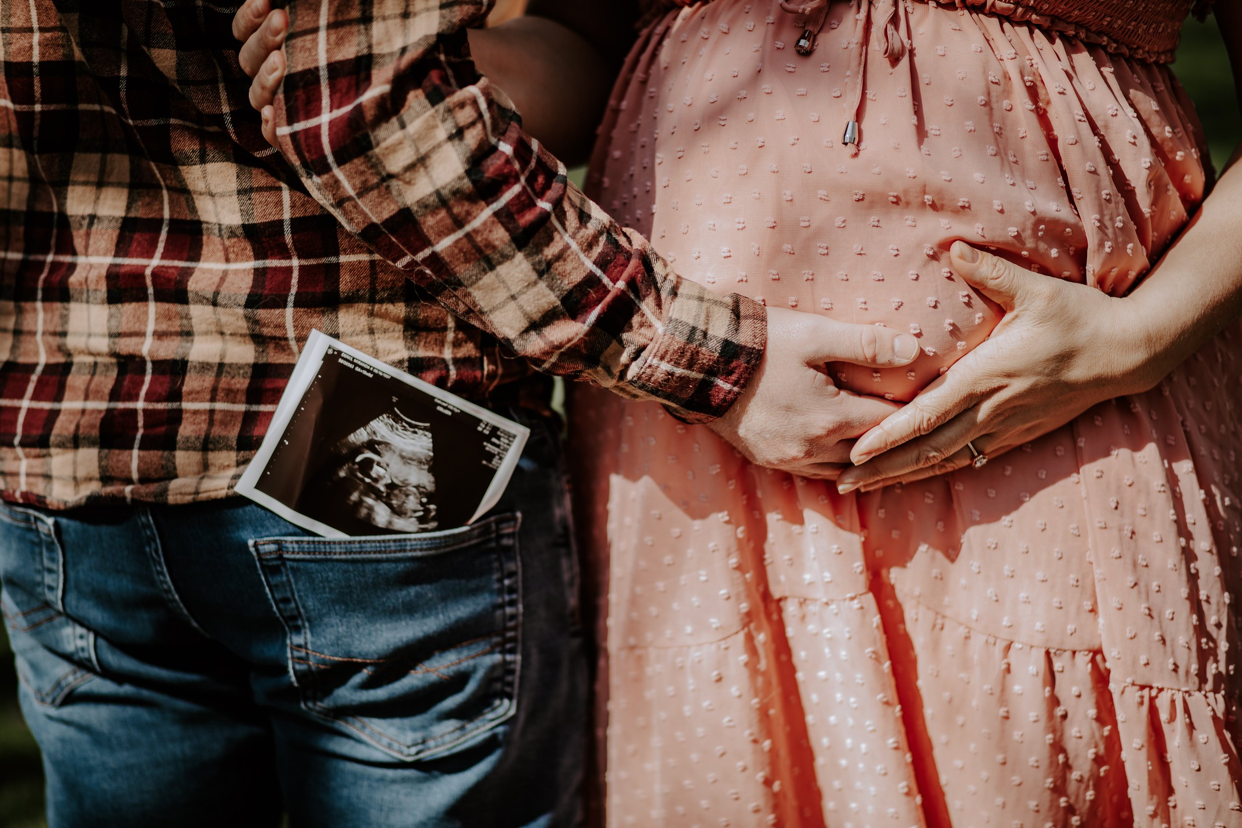 man holding pregnant woman belly with sonogram in back pocket
