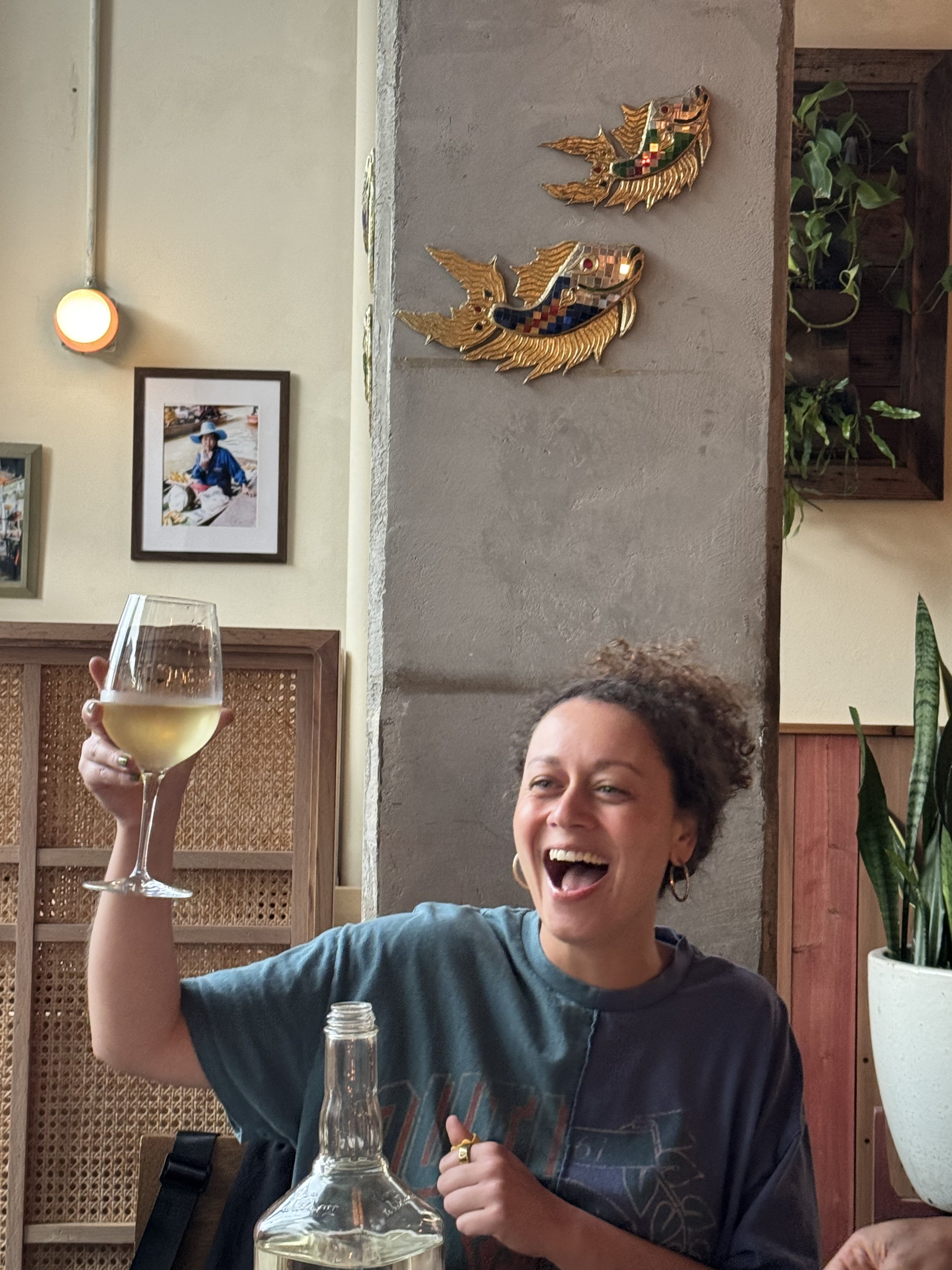 Oregon elopement photographer laughing and raising a glass of wine inside a cozy restaurant.