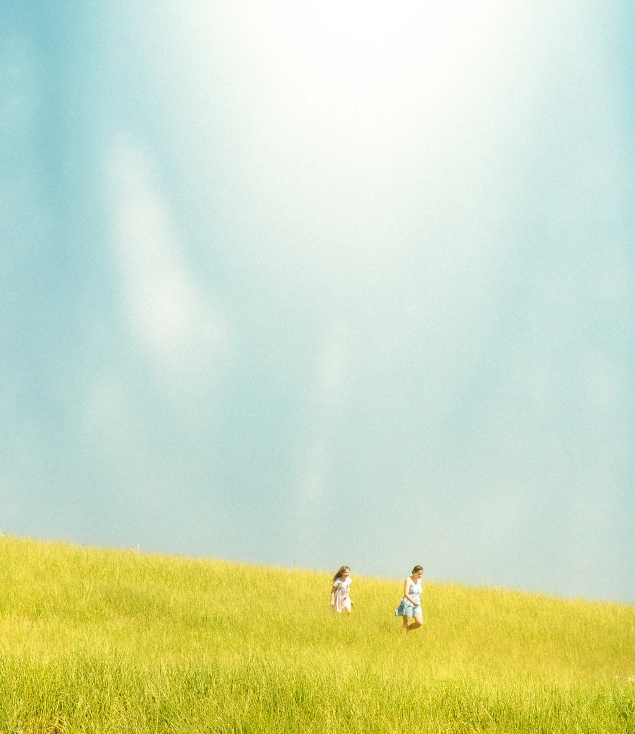 Two young women walking on a grassy hill under a clear blue sky.