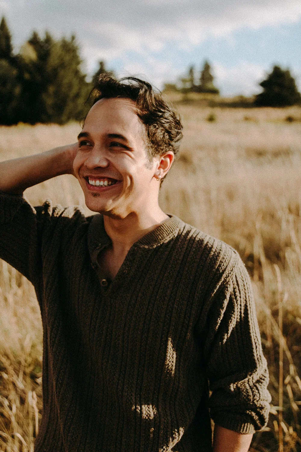 A young man smiling in a wheat field on a sunny day.