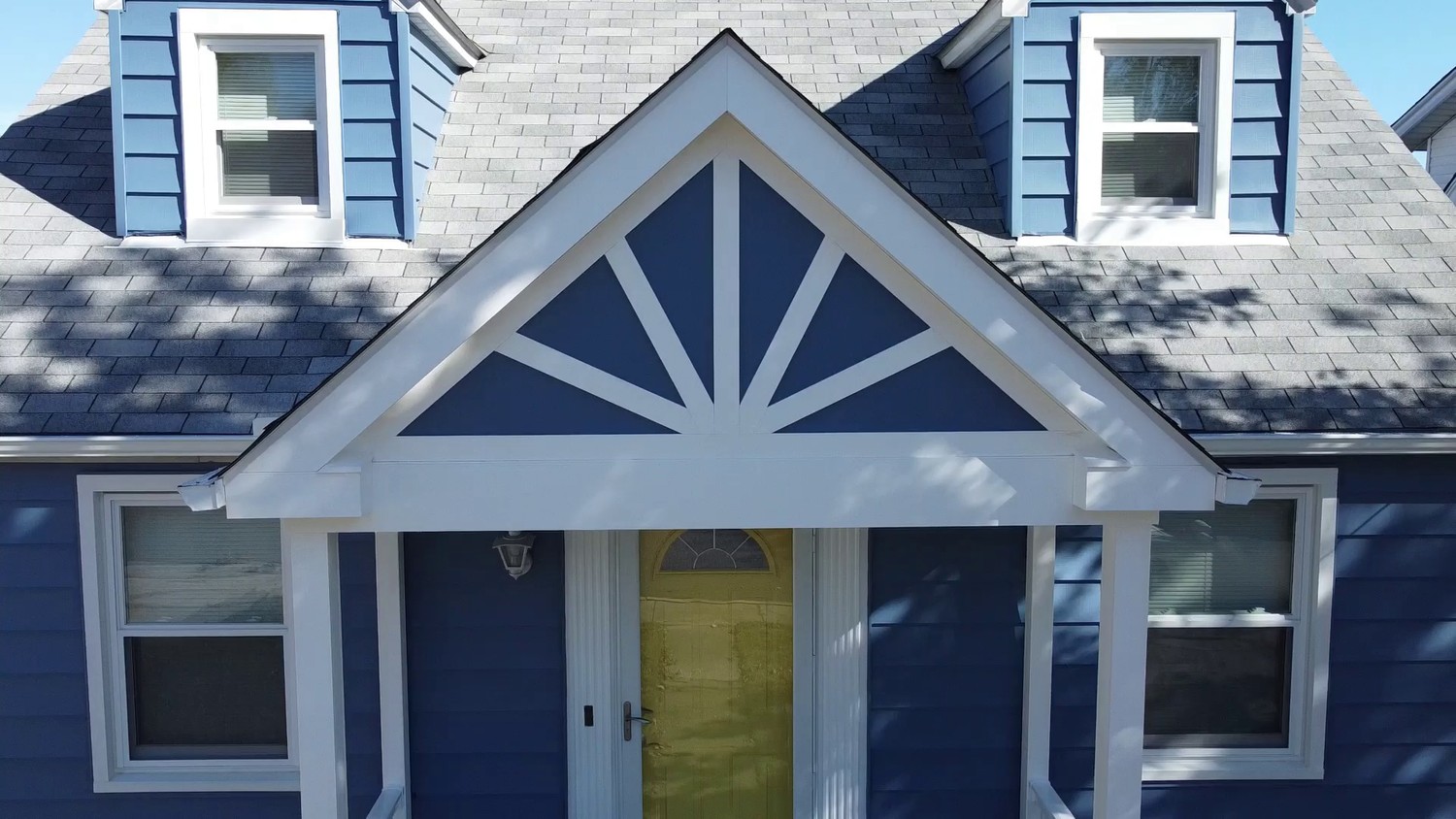 Front porch addition with custom sunburst gable and white trim on blue siding
