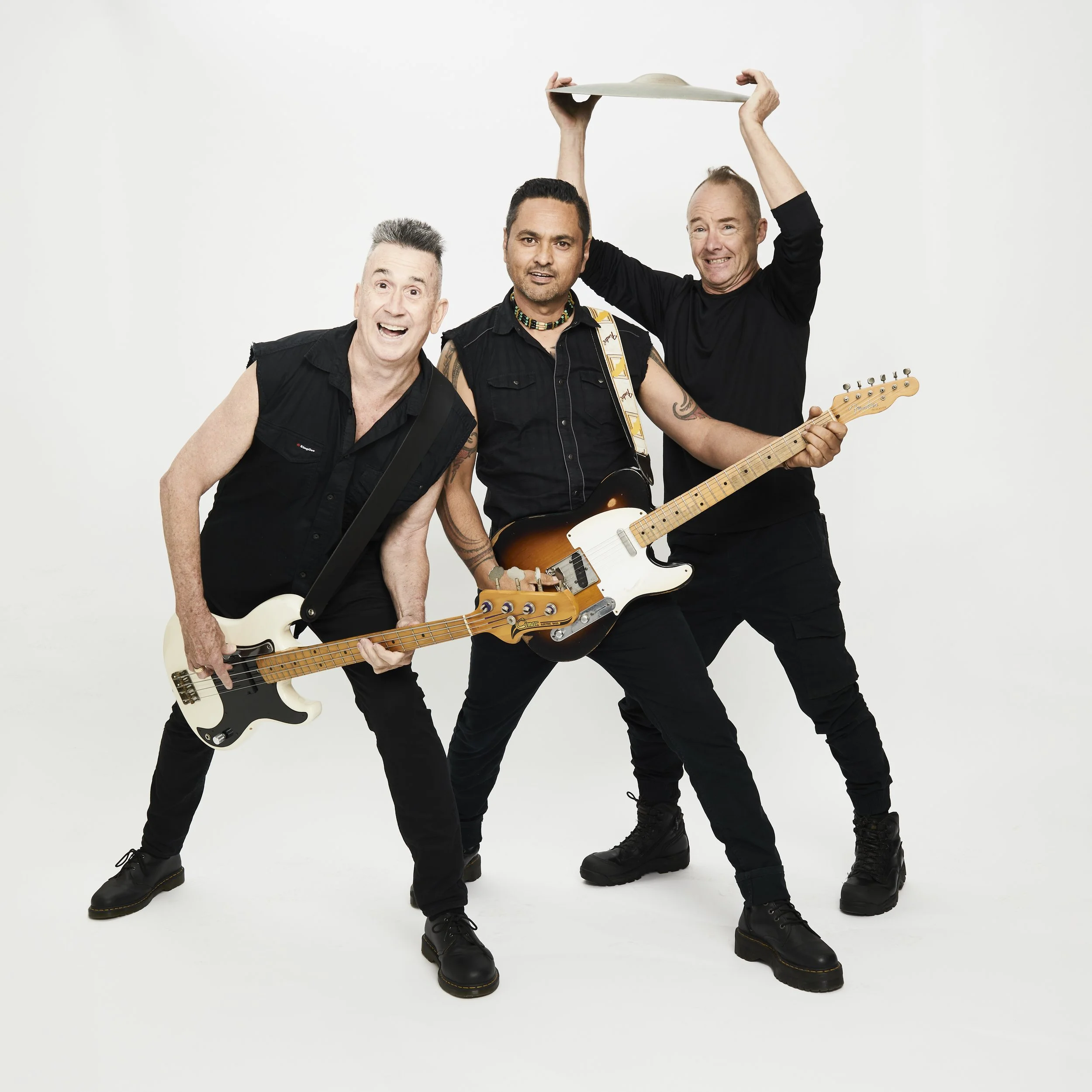 Three men in black outfits, two holding electric guitars, one raising a drum cymbal, against a white background.
