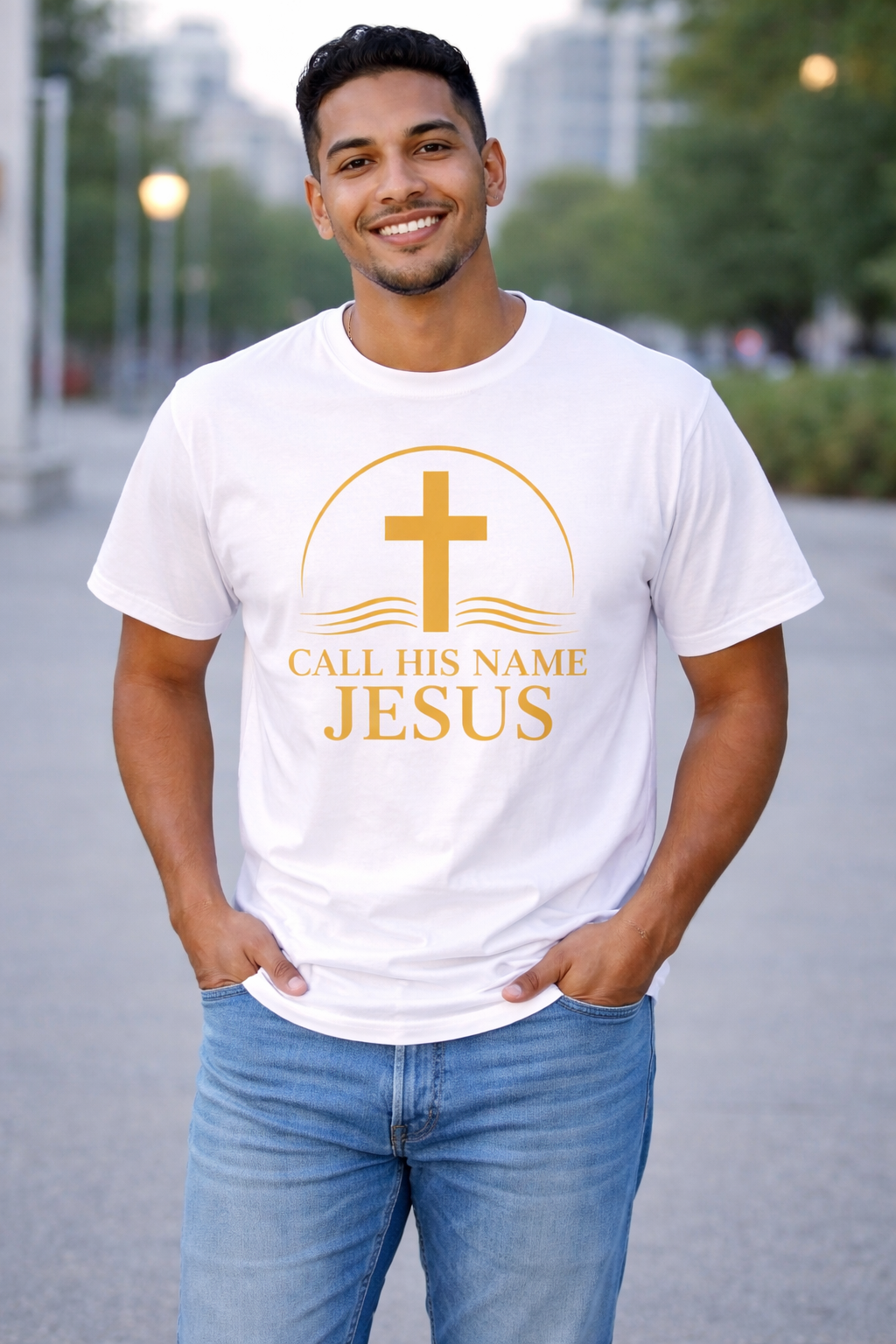 Man wearing white “Call His Name Jesus” t-shirt by Michelle Shearer with gold design in outdoor setting