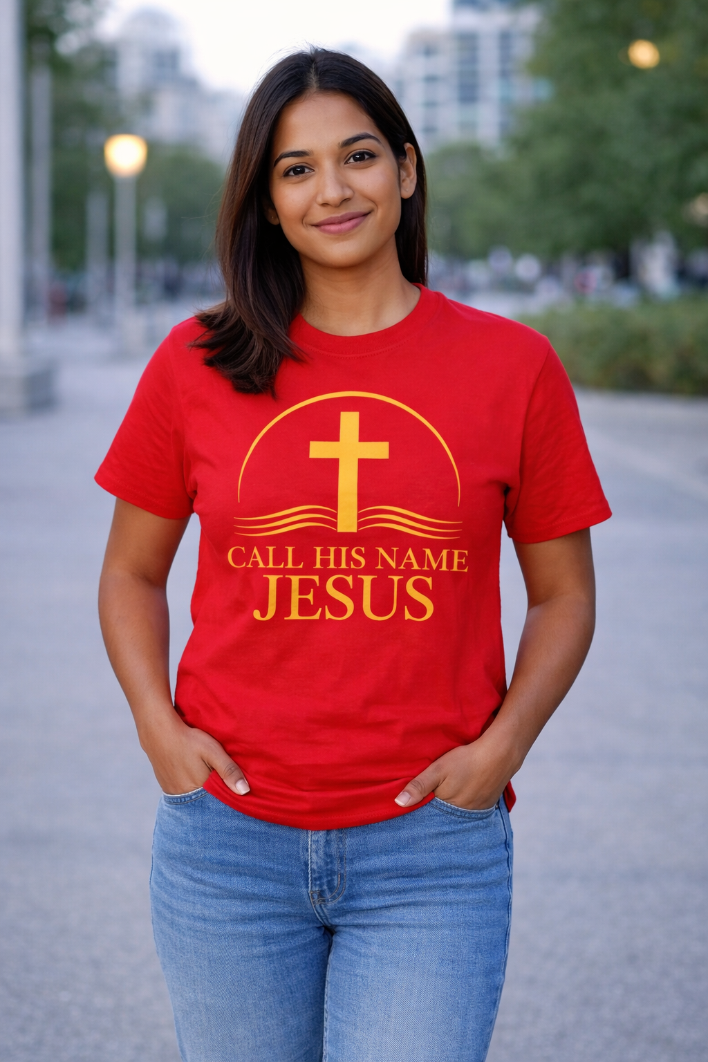 Woman wearing red “Call His Name Jesus” t-shirt by Michelle Shearer with gold design in outdoor setting