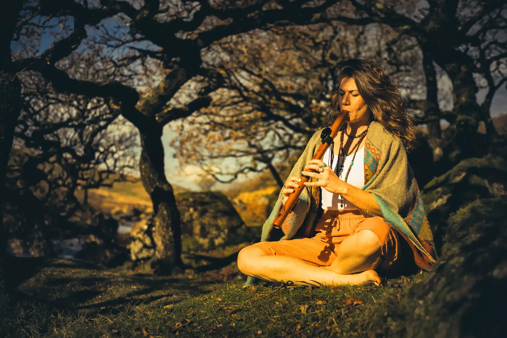 Jessica, a Yoga Teacher & Reiki Master playing the flute in Black-a-Tor Copse on Dartmoor during a portrait photoshoot with Glavind Strachan Photography