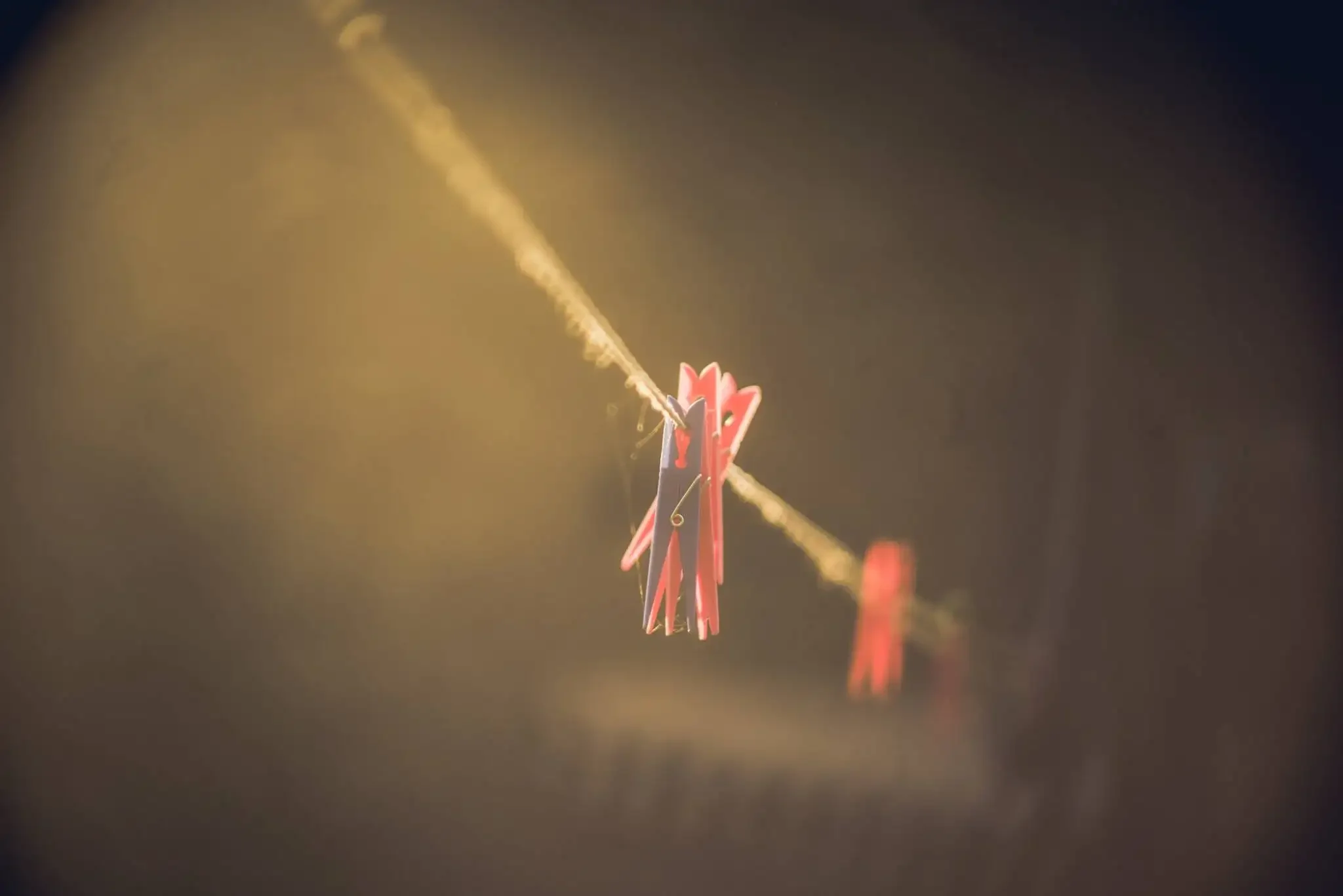 Clothespins hanging on a clothesline with sunlight or warm light shining on them.