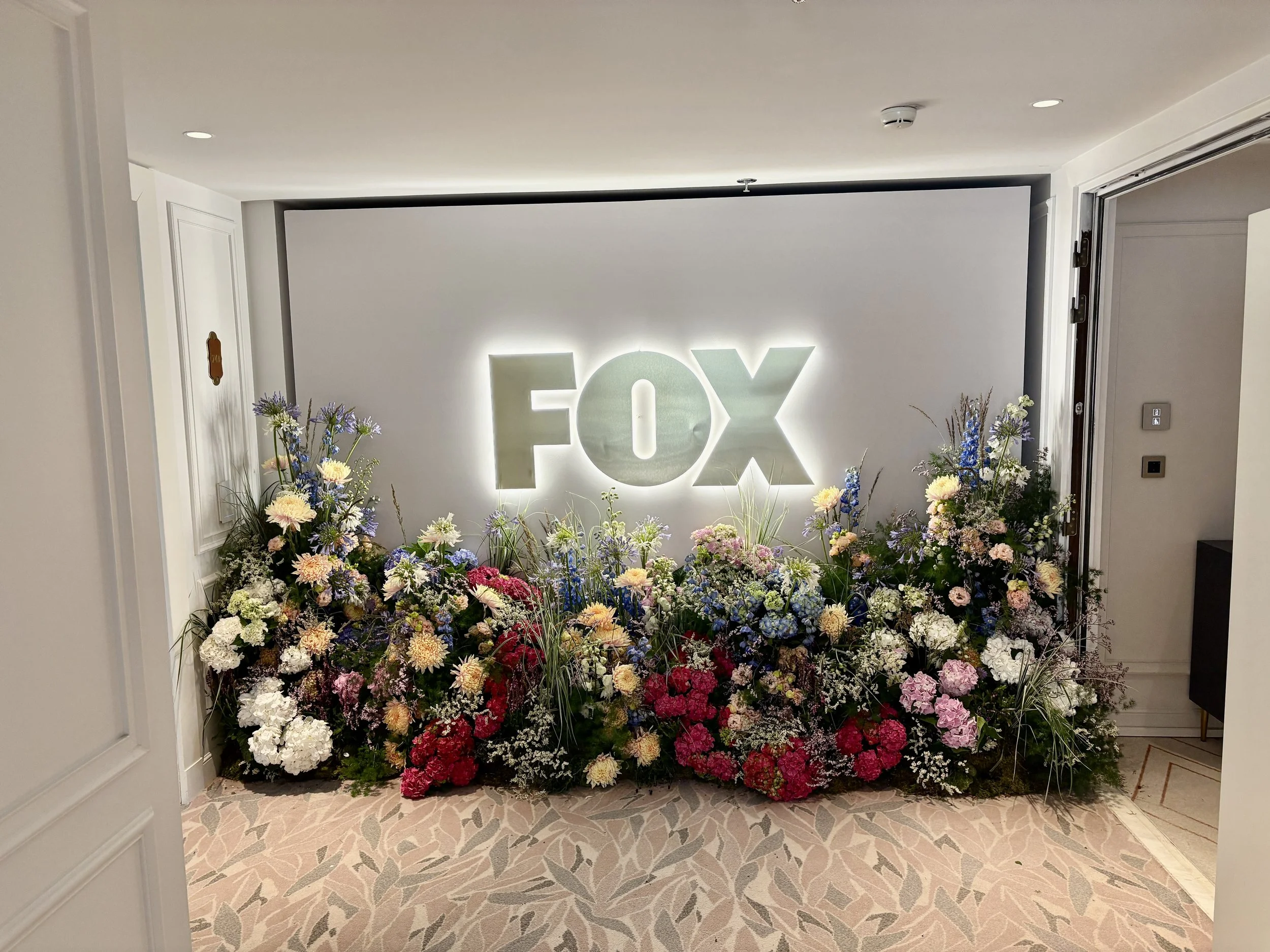 Luxury floral backdrop surrounding the FOX logo at the Ritz-Carlton Suite, featuring abundant premium blooms for an exclusive VIP event with modern botanical styling