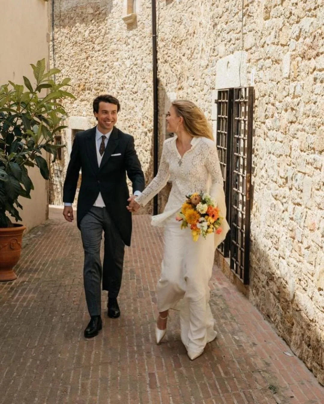 Bride and groom walking hand in hand in Costa Brava, holding a bespoke bouquet designed by Mosaic for their luxury wedding