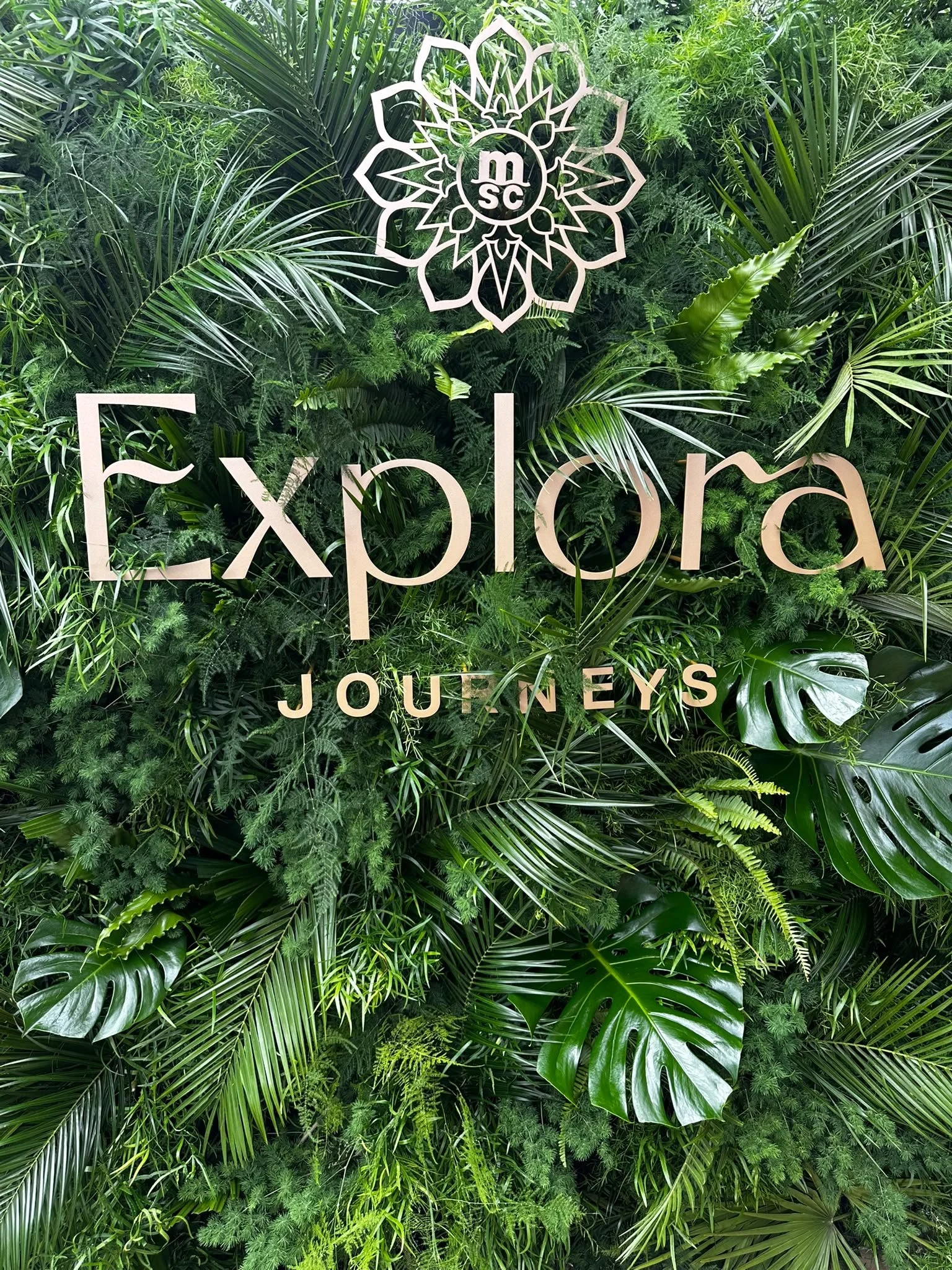 Luxury fresh foliage backdrop with the Explora Journeys logo handcrafted by Mosaic Flowers