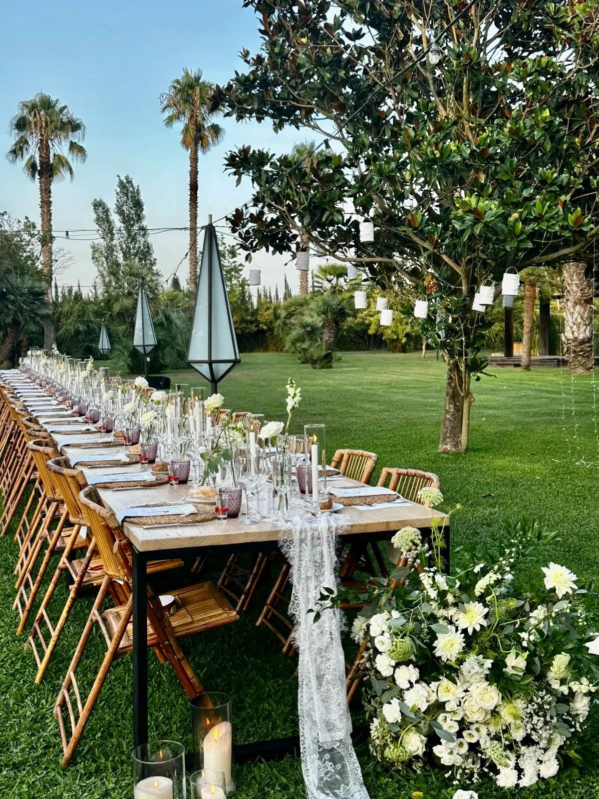 A sophisticated outdoor dining installation created by Mosaic at Cortal Gran, with cascading white florals, lace-like textile details, candlelight and an elegant Mediterranean garden setting