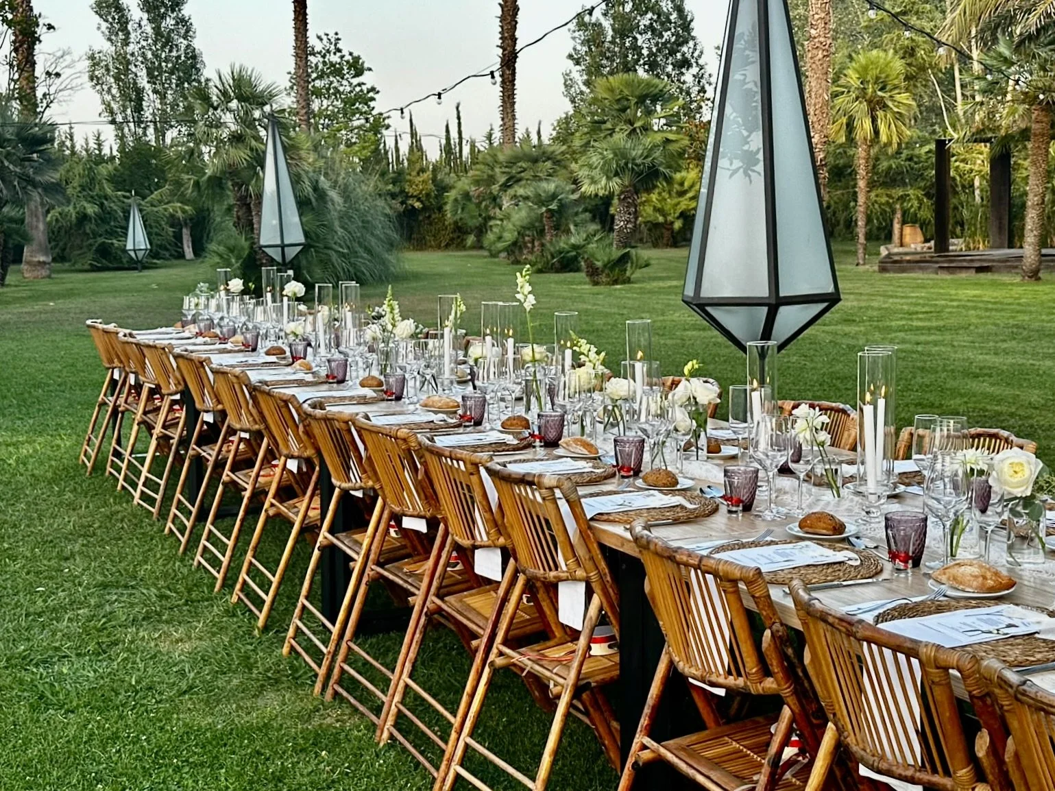 A long outdoor wedding table framed by Mosaic’s floral scenography at Cortal Gran, with abundant white flowers, natural greenery, candles and warm wooden seating across the garden