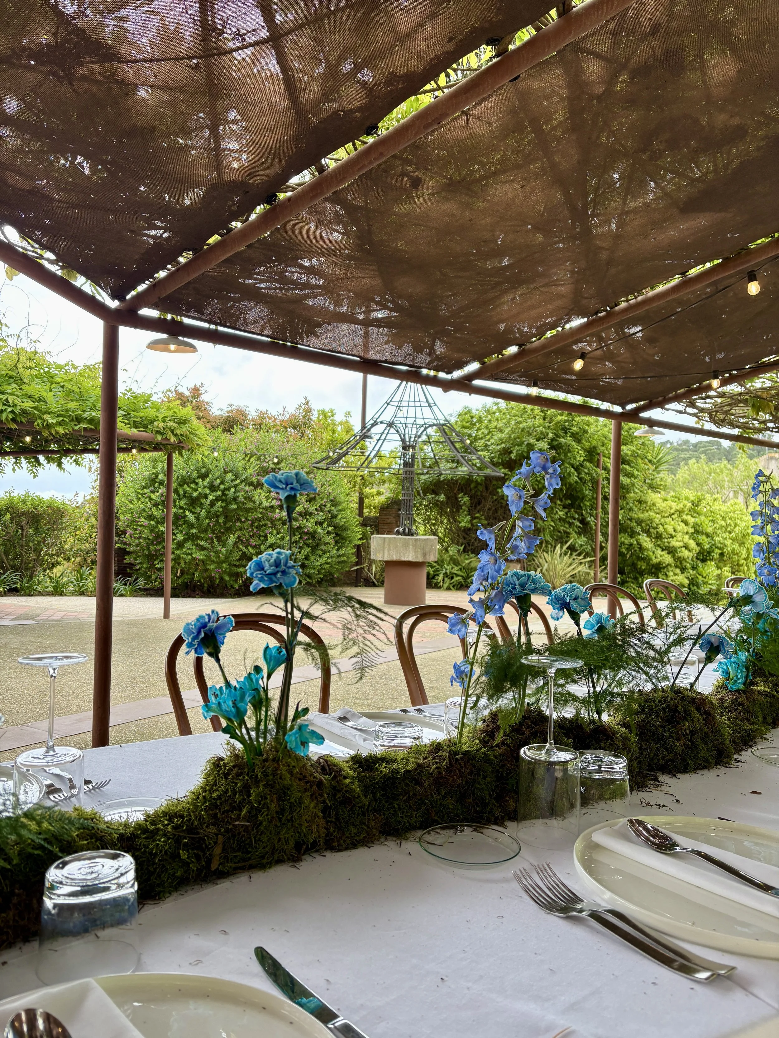 Contemporary floral tablescape featuring a bespoke moss runner and striking blue blooms, created for an exclusive ASICS brand event in a luxury masia near Barcelona