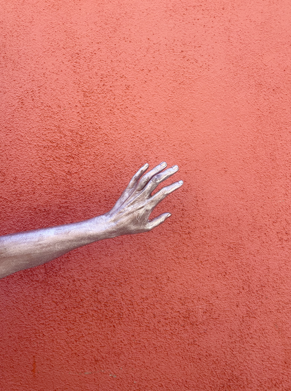 Silver-painted hand against a pink wall, artistic floral installation detail by Mosaic