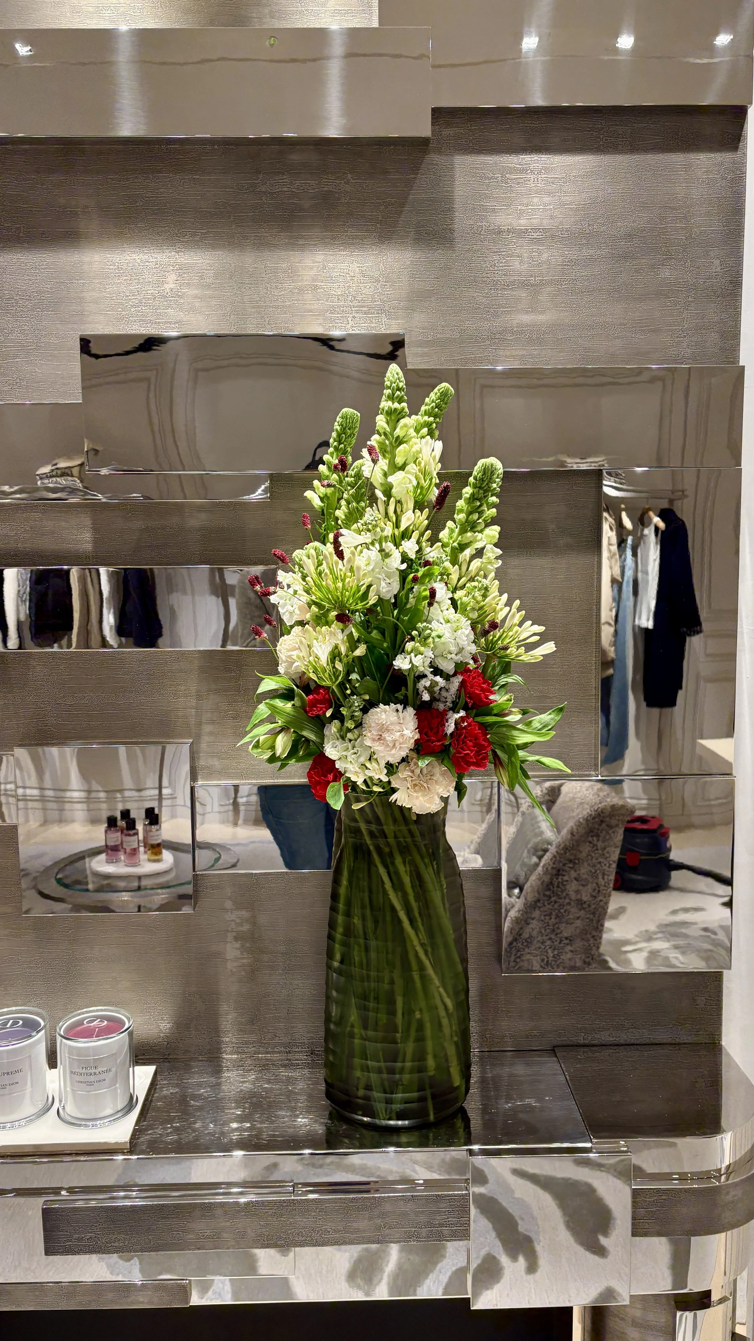 Elegant luxury floral arrangement in a tall green glass vase created for a Barcelona flagship boutique during the Spring Summer 2027 collection launch
