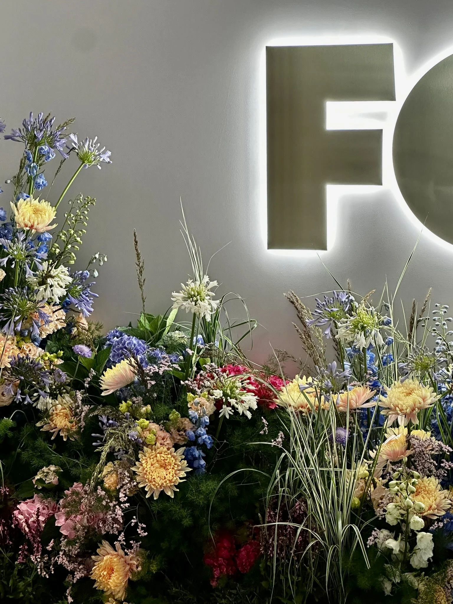 Contemporary floral installation framing illuminated FOX signage at the Ritz-Carlton Suite, designed with luxury seasonal flowers for a premium VIP brand experience