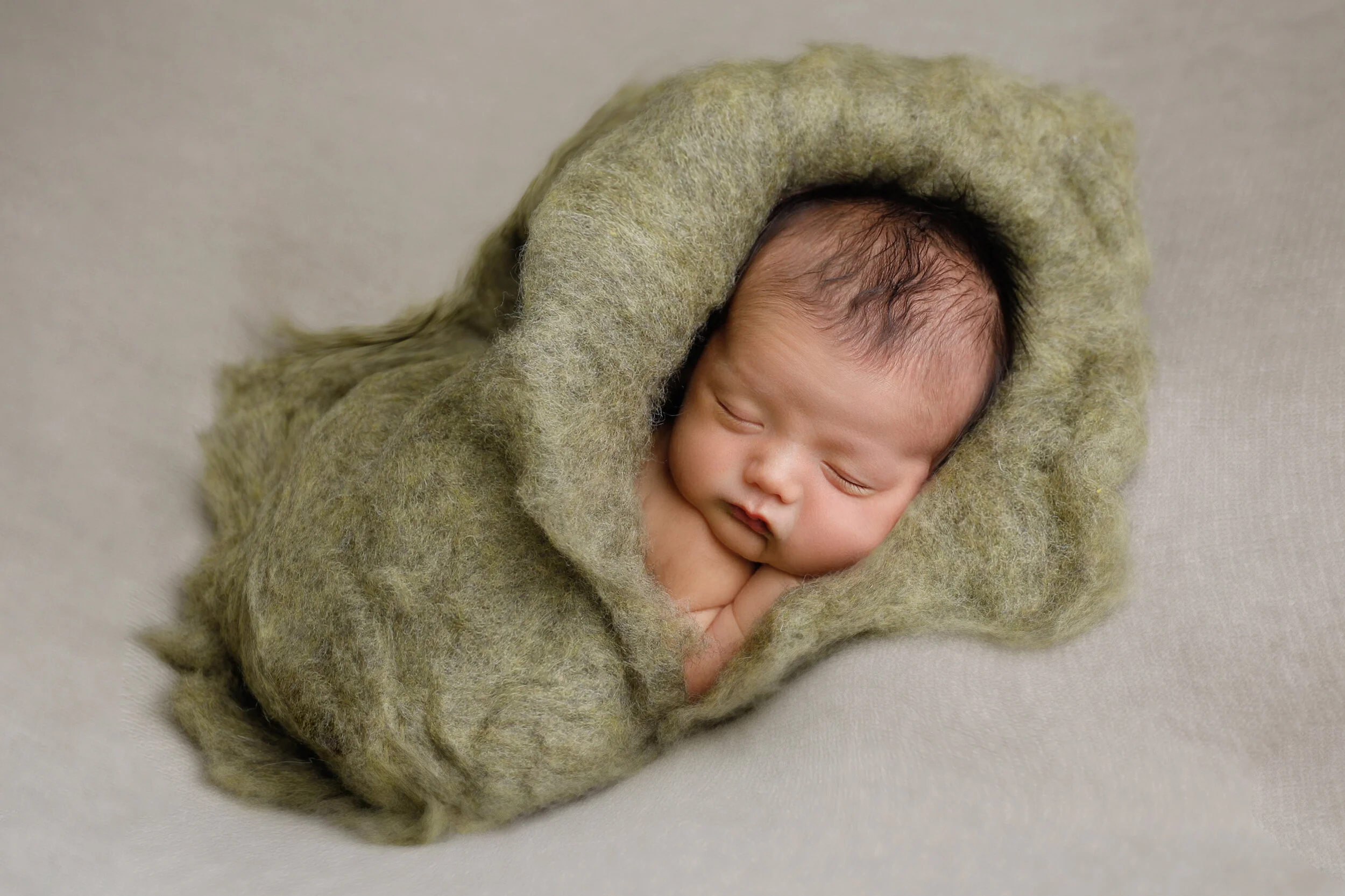 Sleeping newborn baby wrapped in soft green blanket on light-colored surface.
