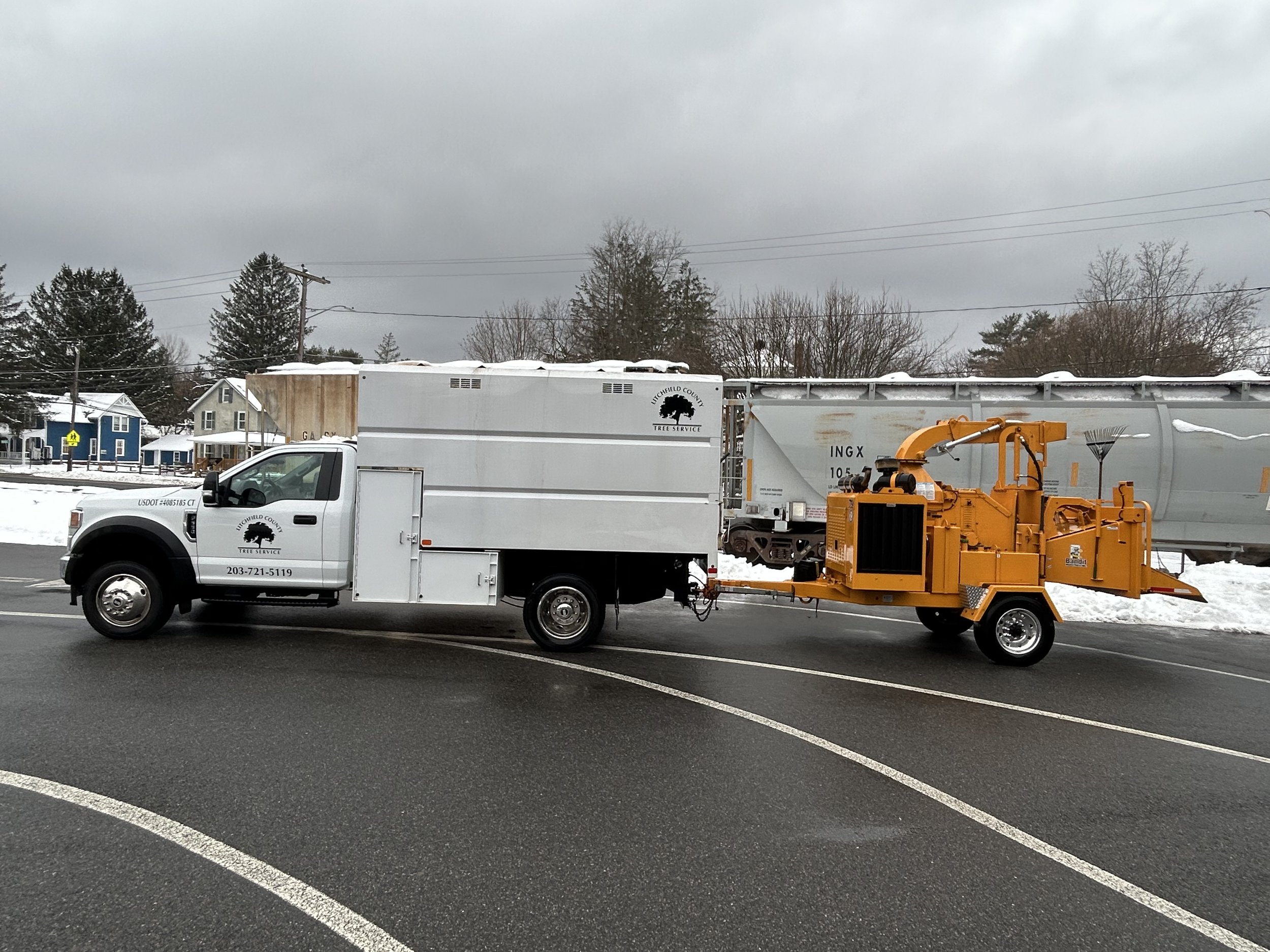 Tree service truck with a wood chipper attachment on a road with snow, in a residential area.