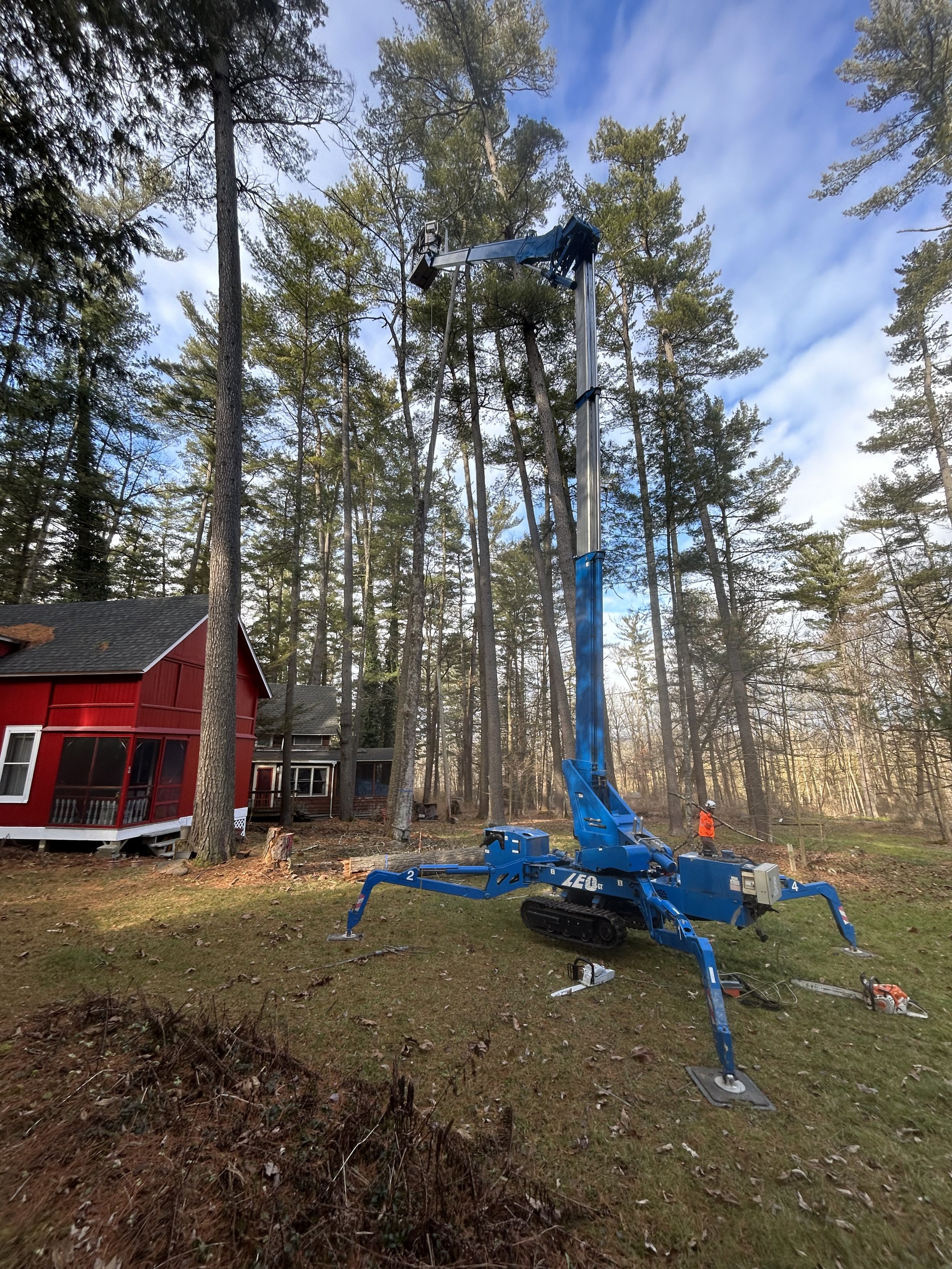 A blue cherry picker lift in a backyard surrounded by trees with a red house nearby.