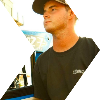 A young man with a baseball cap and black t-shirt, sitting indoors near a window.