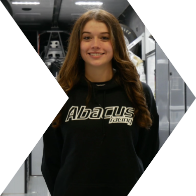 Smiling young woman with long brown hair wearing a black hoodie with 'Abacus Racing' logo, standing in a technology or industrial environment.