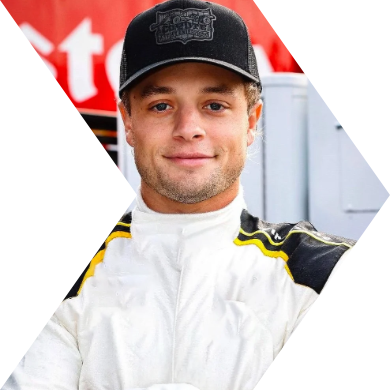 A young male race car driver taking a selfie, wearing a white racing suit with black and yellow accents and a black cap.