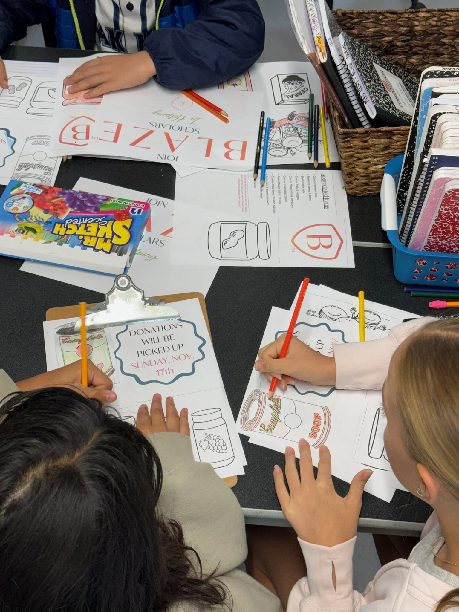 Children working on food donation posters at a table with coloring sheets and markers.