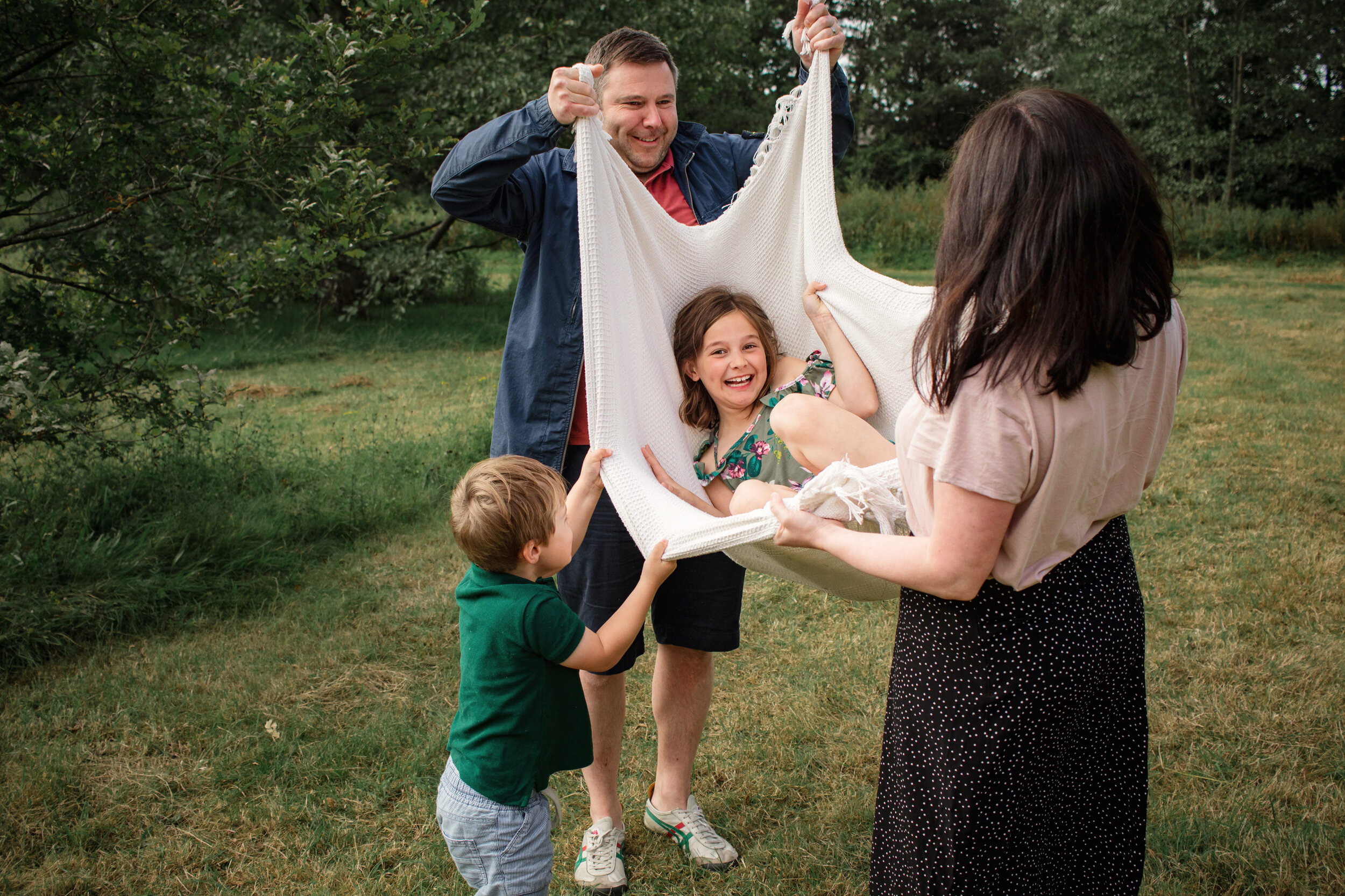 parents lift smiling young girl in a blanket while little boy pears over during a family session