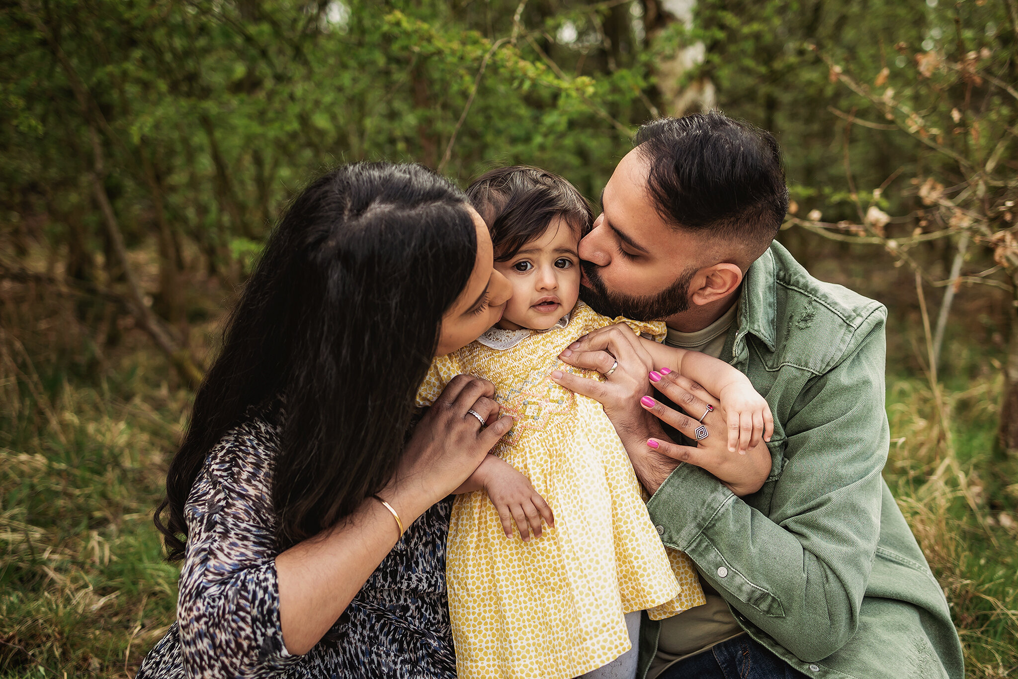 Mum and Dad kiss little girl on her cheeks during family photos of an outdoor cake smash session in Derby