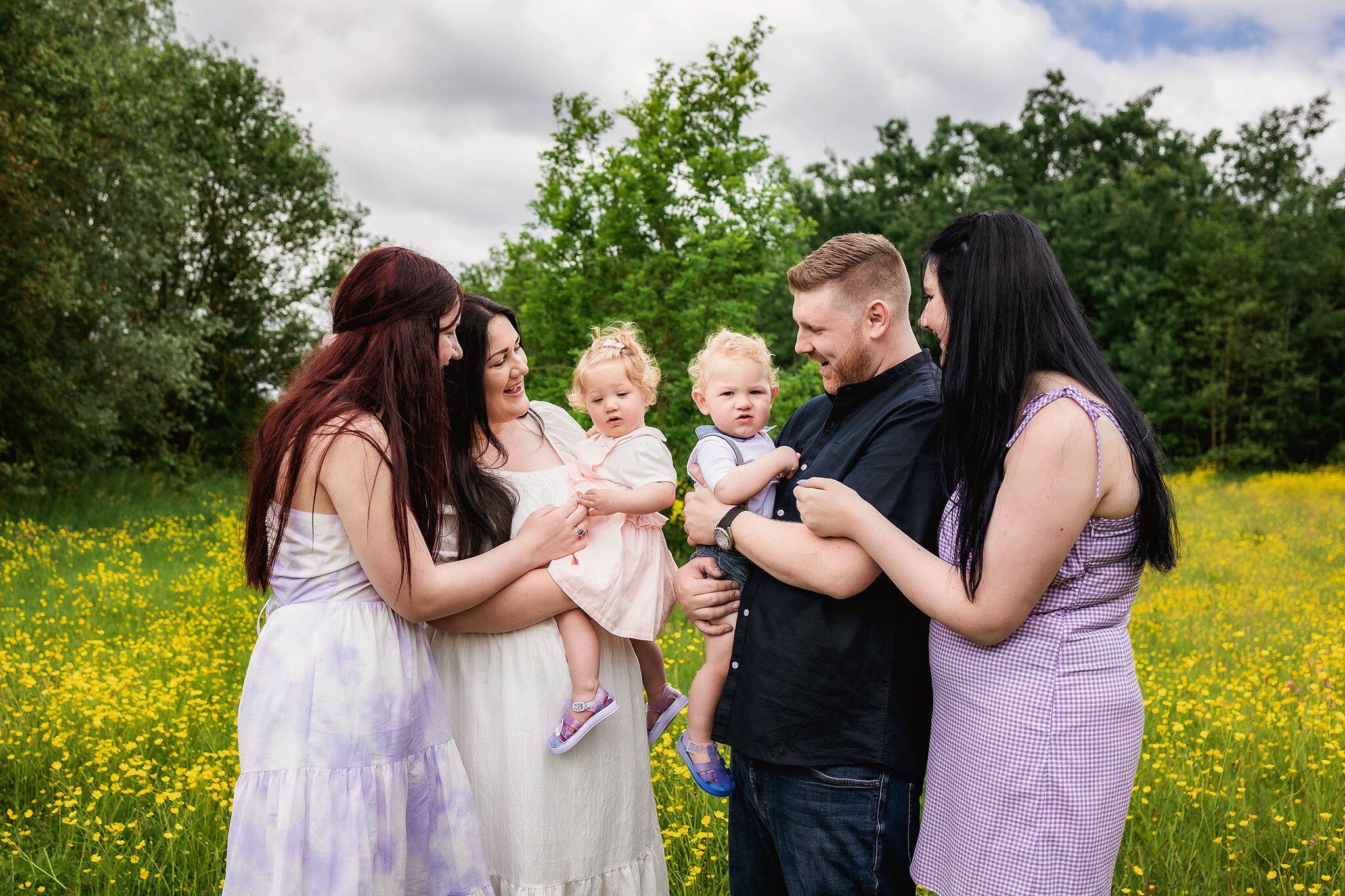 Large family snuggle in close together to play with one year old twins during family photos of an outdoor cake smash session in Derby