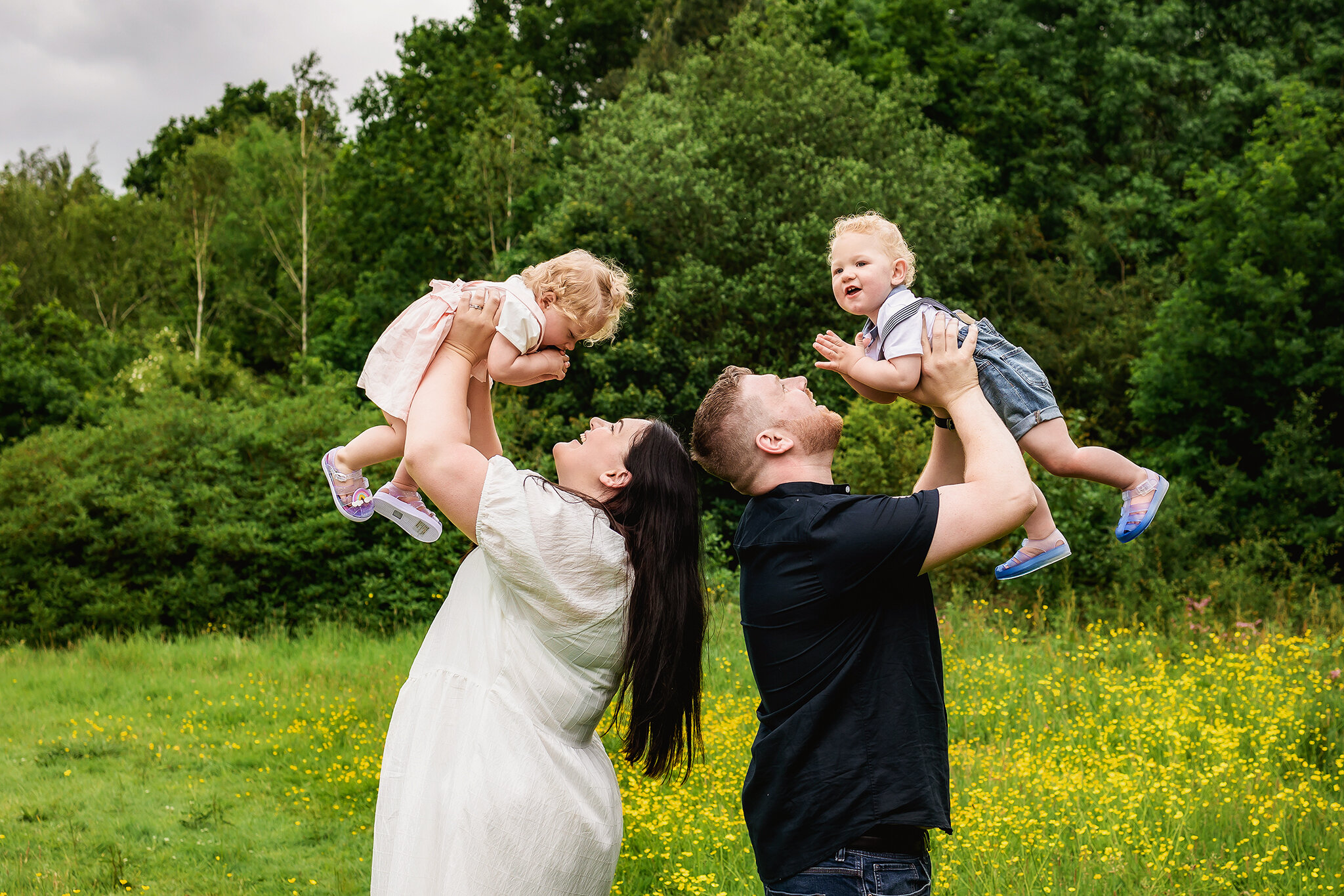 Mum and Dad lift one year old twins in the air during family photos of an outdoor cake smash session in Derby