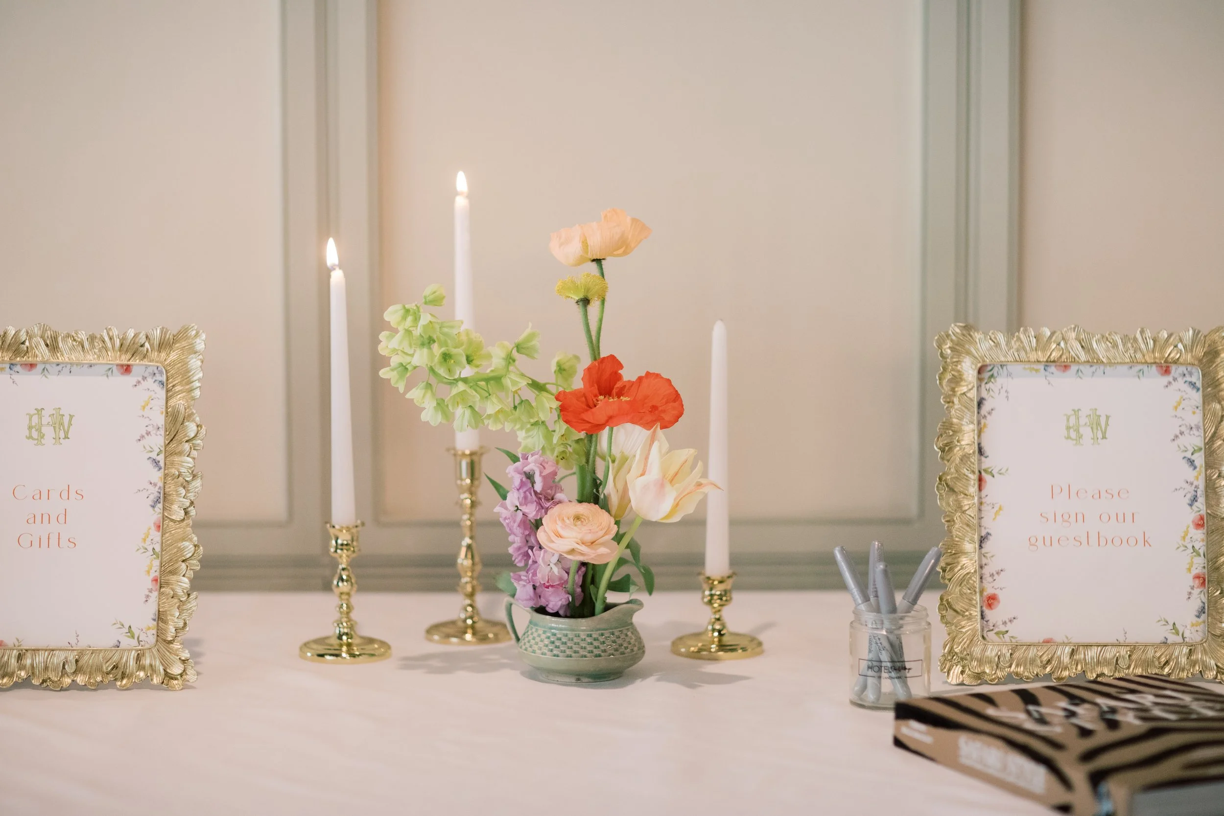 Table for guests with a floral centerpiece, lit candles, guestbook sign, and sign-in pens.