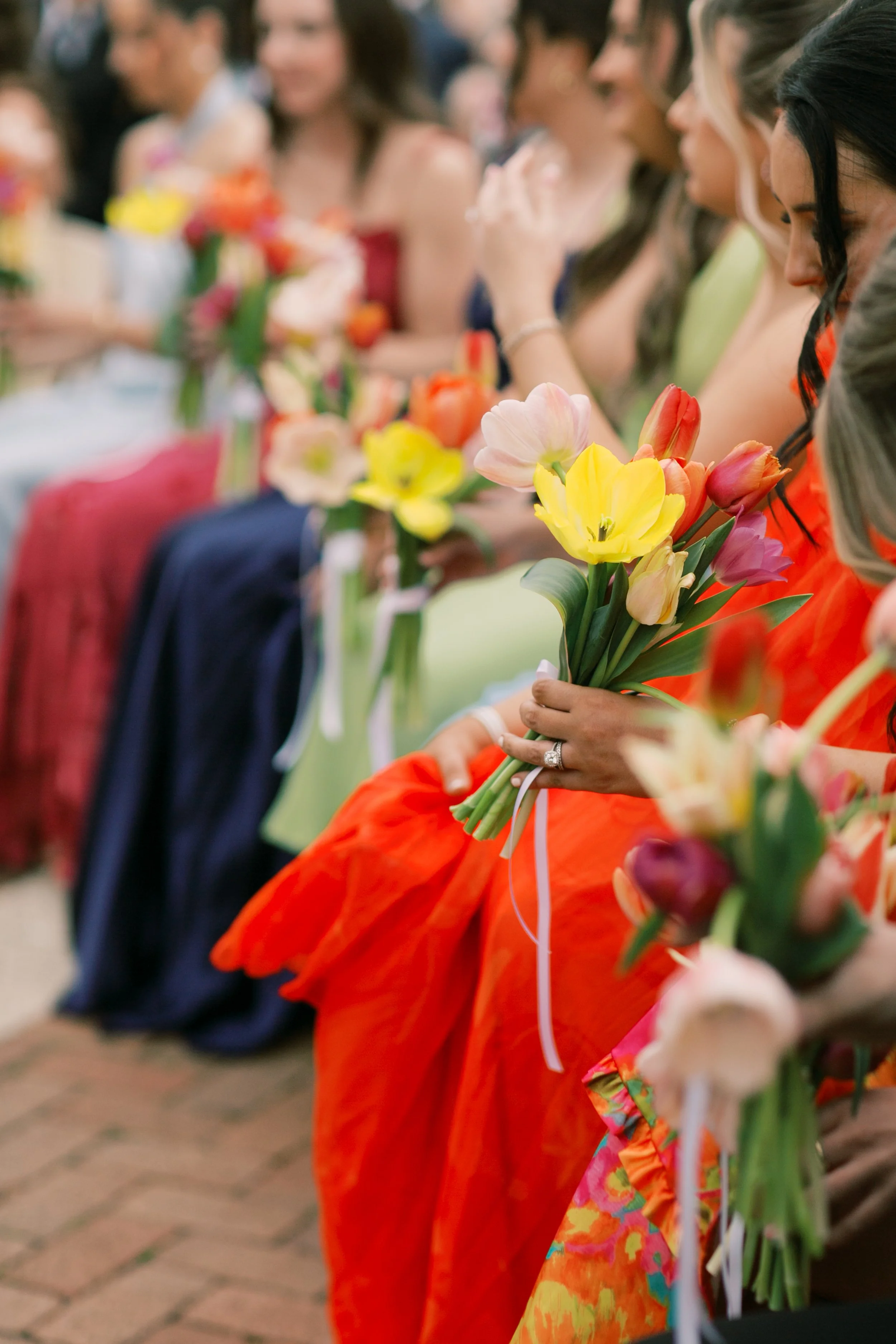 Bridesmaids in colorful dresses holding bouquets of tulips at a wedding.