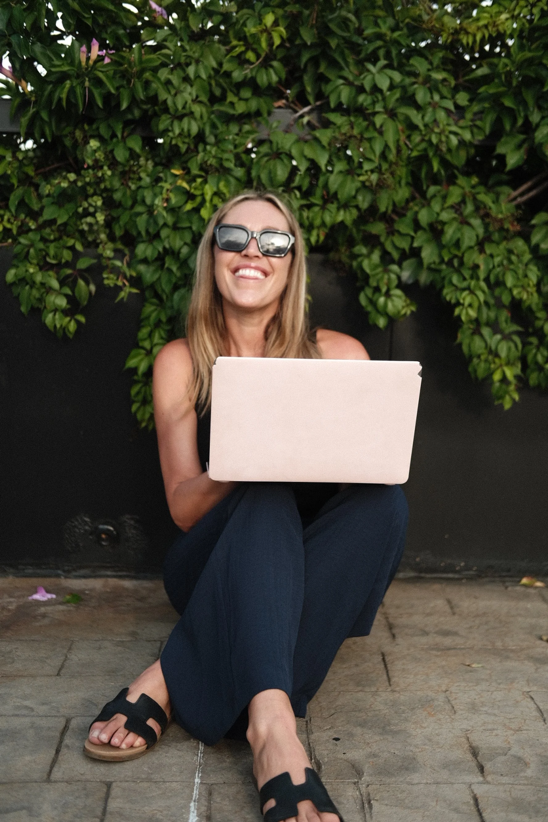 Person with long blonde hair holds a teal bag and a book on a city street.