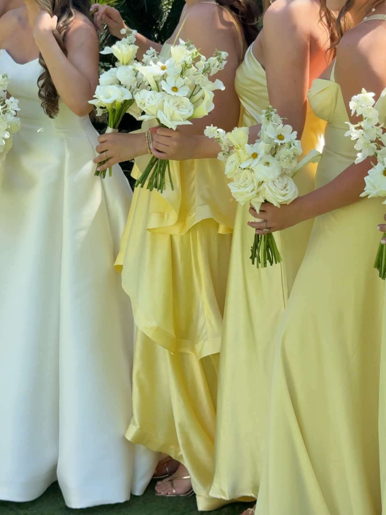 Group of women in pastel-colored dresses holding white floral bouquets at a wedding or celebration.