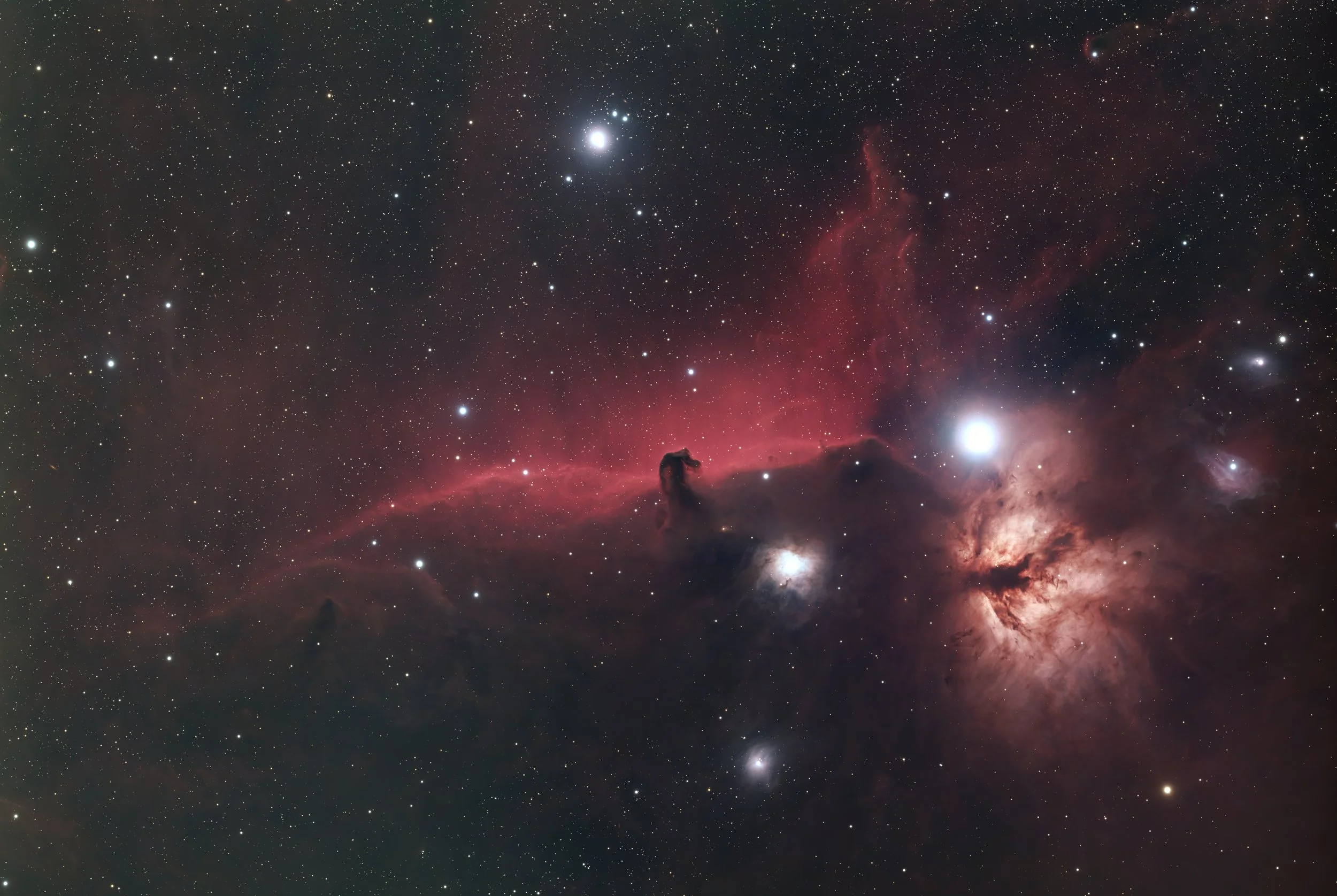 A detailed image of outer space featuring numerous stars, nebulae, and celestial objects with some areas highlighted by reddish and pinkish gas clouds.