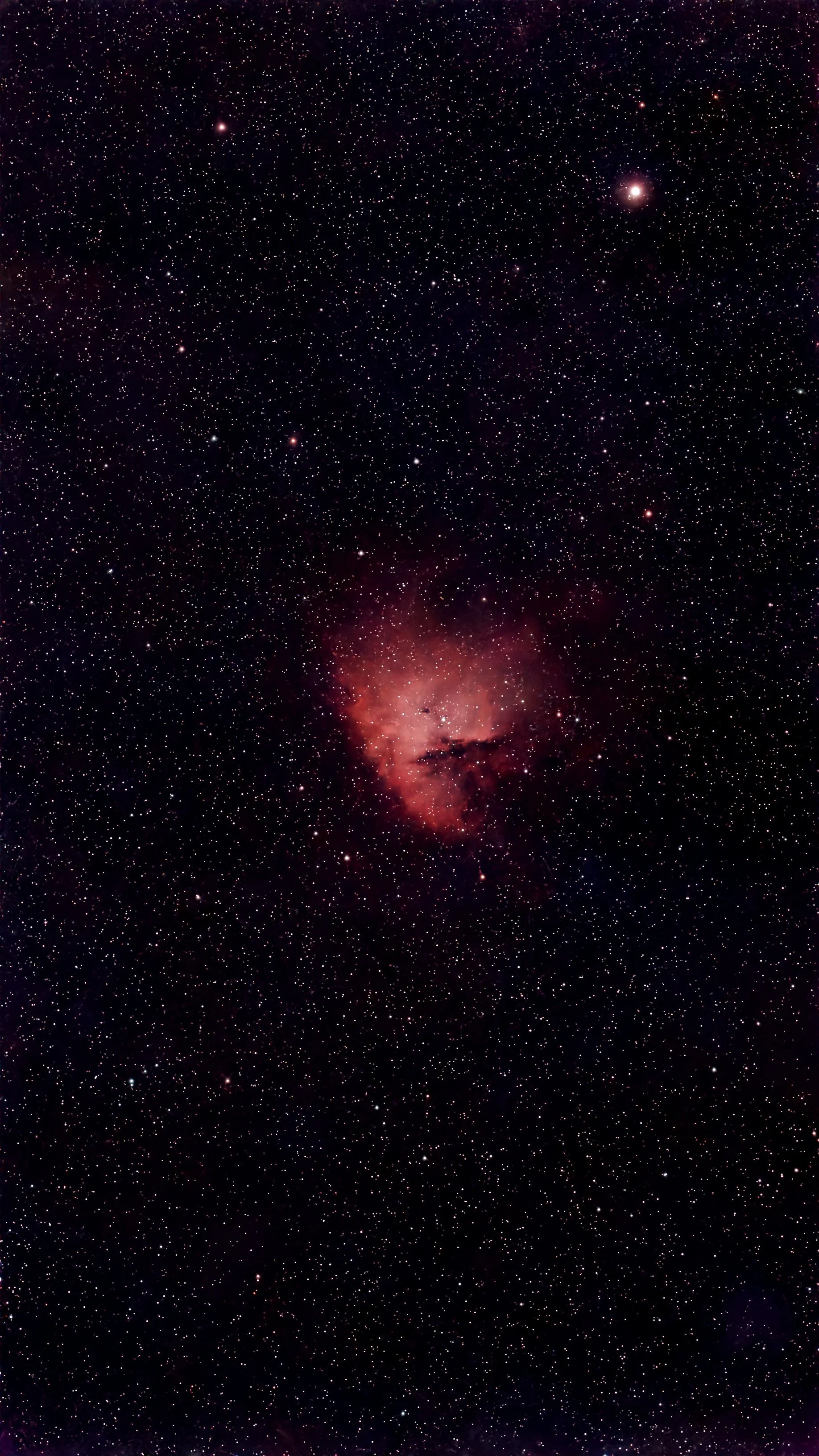 A photograph of the night sky filled with countless stars and a bright pink nebula near the bottom.