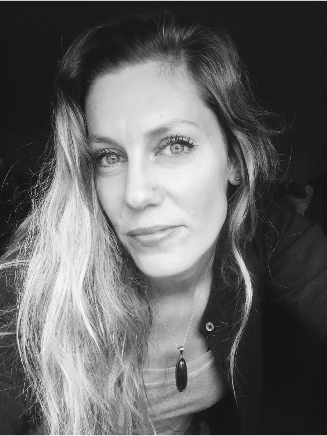 Black and white portrait of a woman with long hair, wearing a necklace and a cardigan.