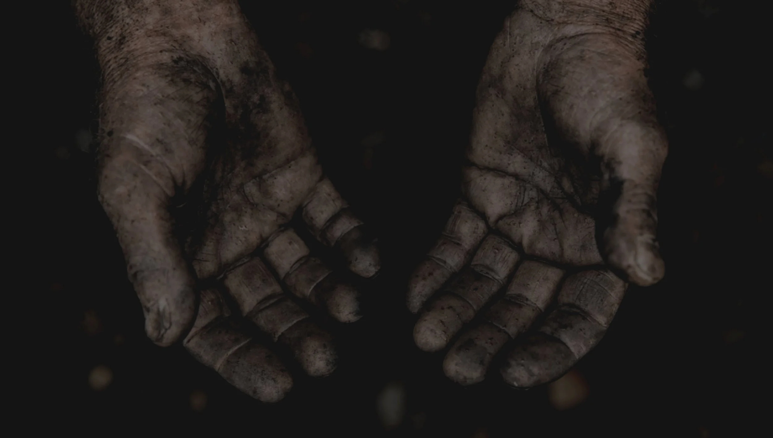Dirty, muddy hands with palms facing upward against a dark background.