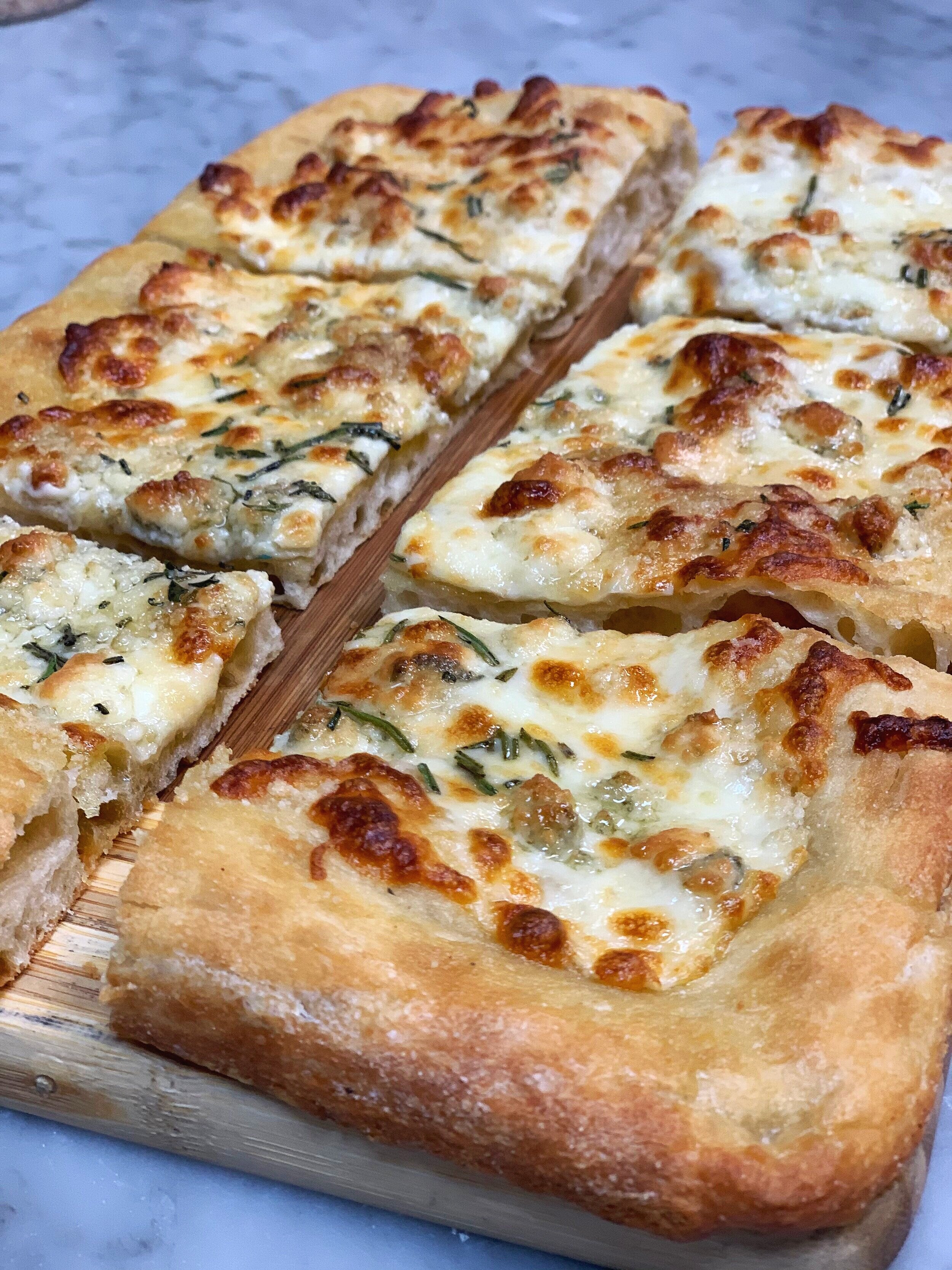 Four slices of white pizza with cheese, herbs, and a thick crust on a wooden cutting board.