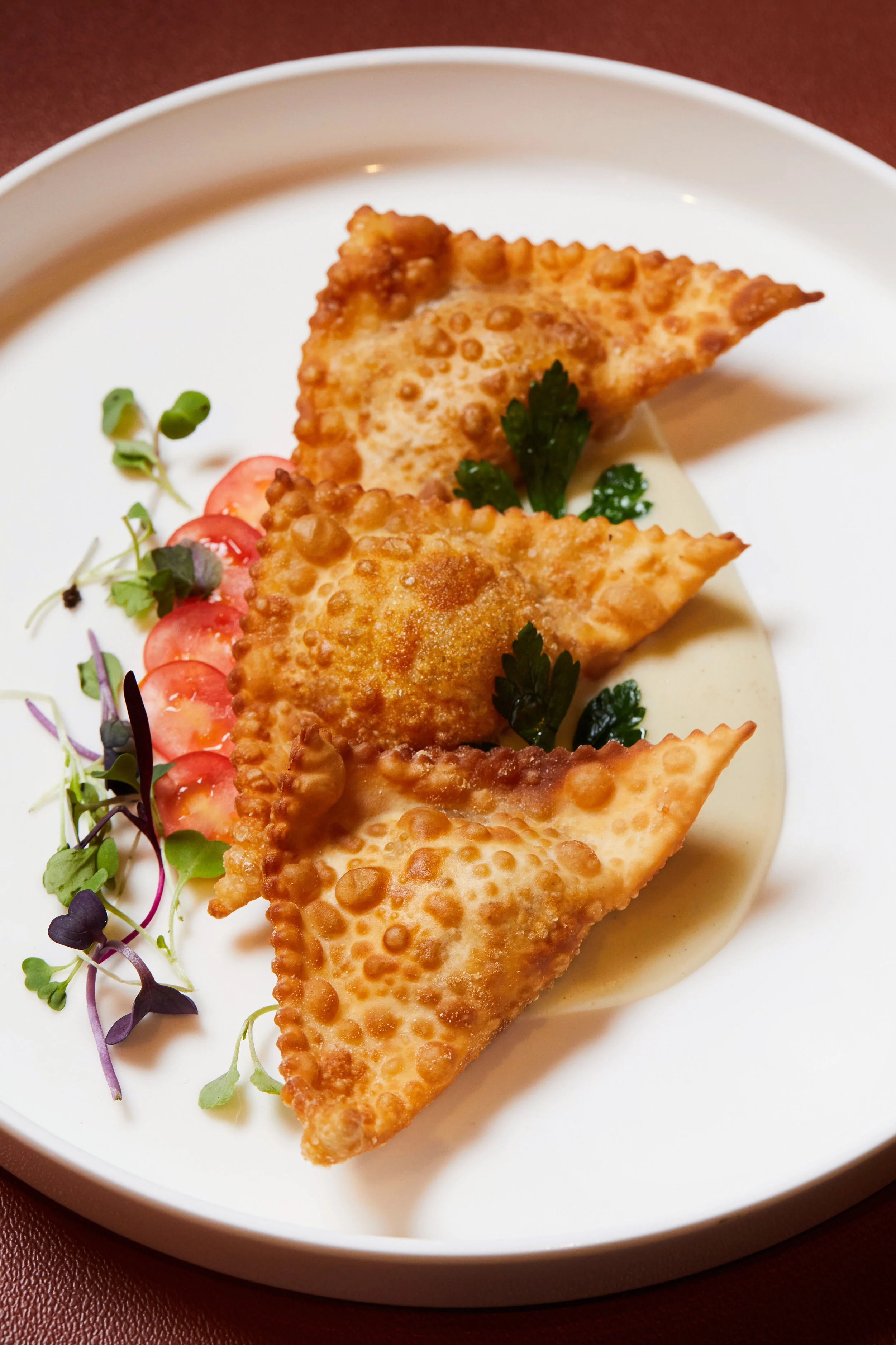 Crispy panzerotti garnished with parsley, served on a white plate with cherry tomato slices and microgreens, with white dipping sauce.